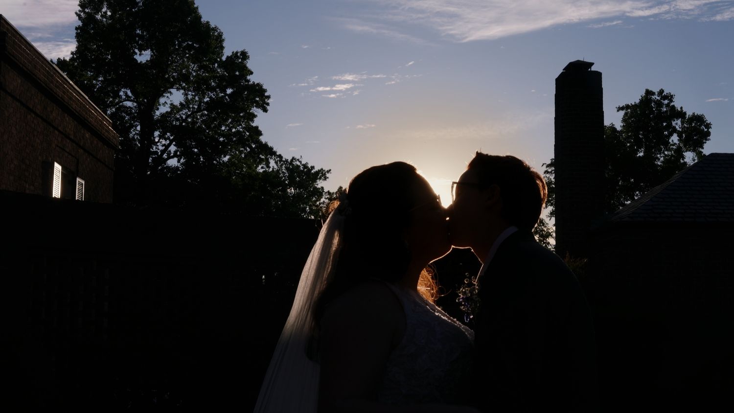 Silhouette of a bride and groom sharing a romantic kiss at sunset with a glowing sky backdrop.