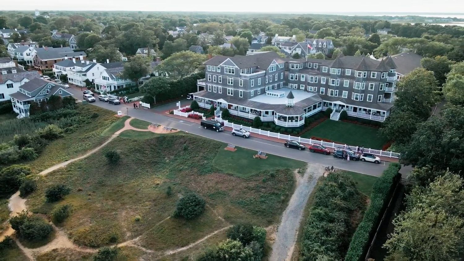 Aerial view of a large historic hotel surrounded by lush trees and green grounds near a coastal New England town.