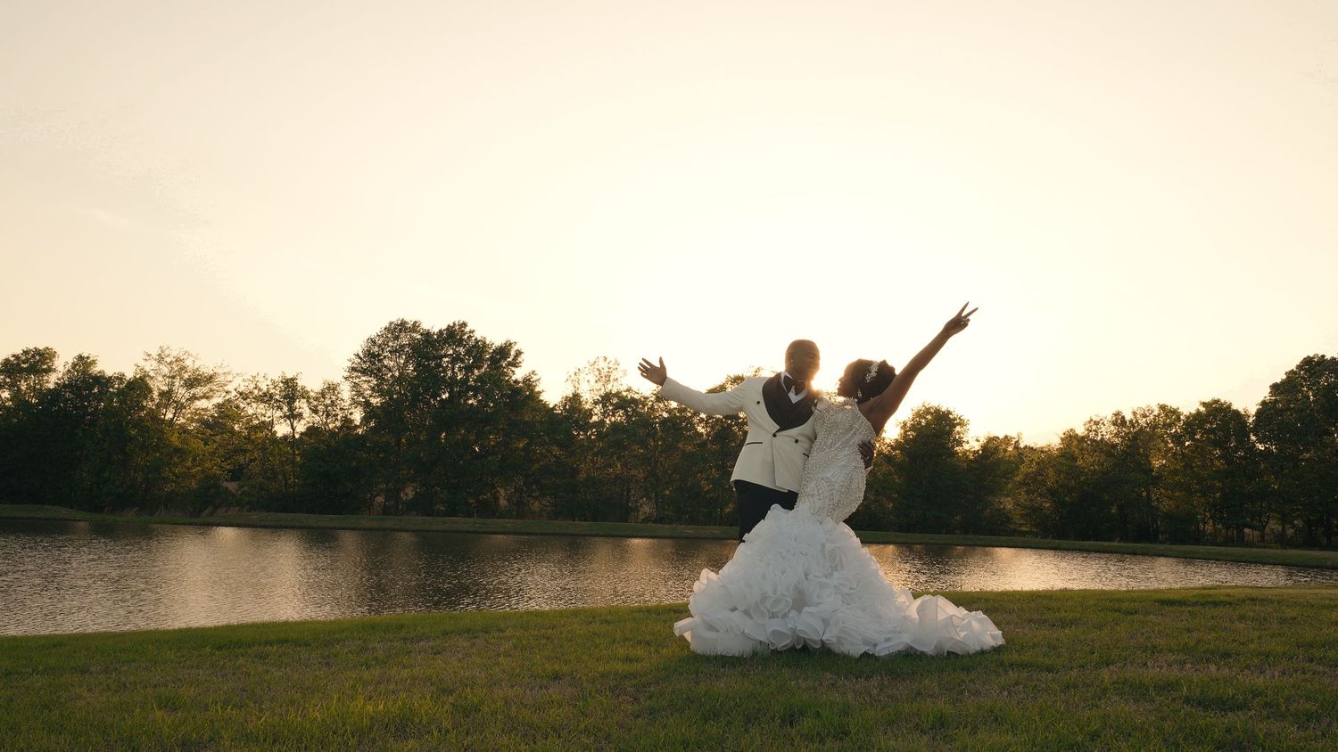 Bride and groom celebrating joyfully by a lake at sunset in a stunning ball gown wedding dress.
