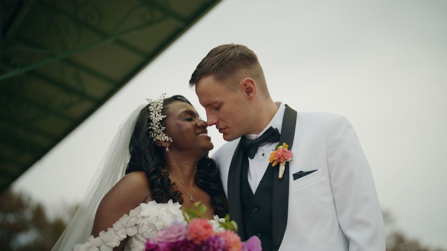 Interracial wedding couple sharing a romantic moment, bride in white gown and groom in white tuxedo.