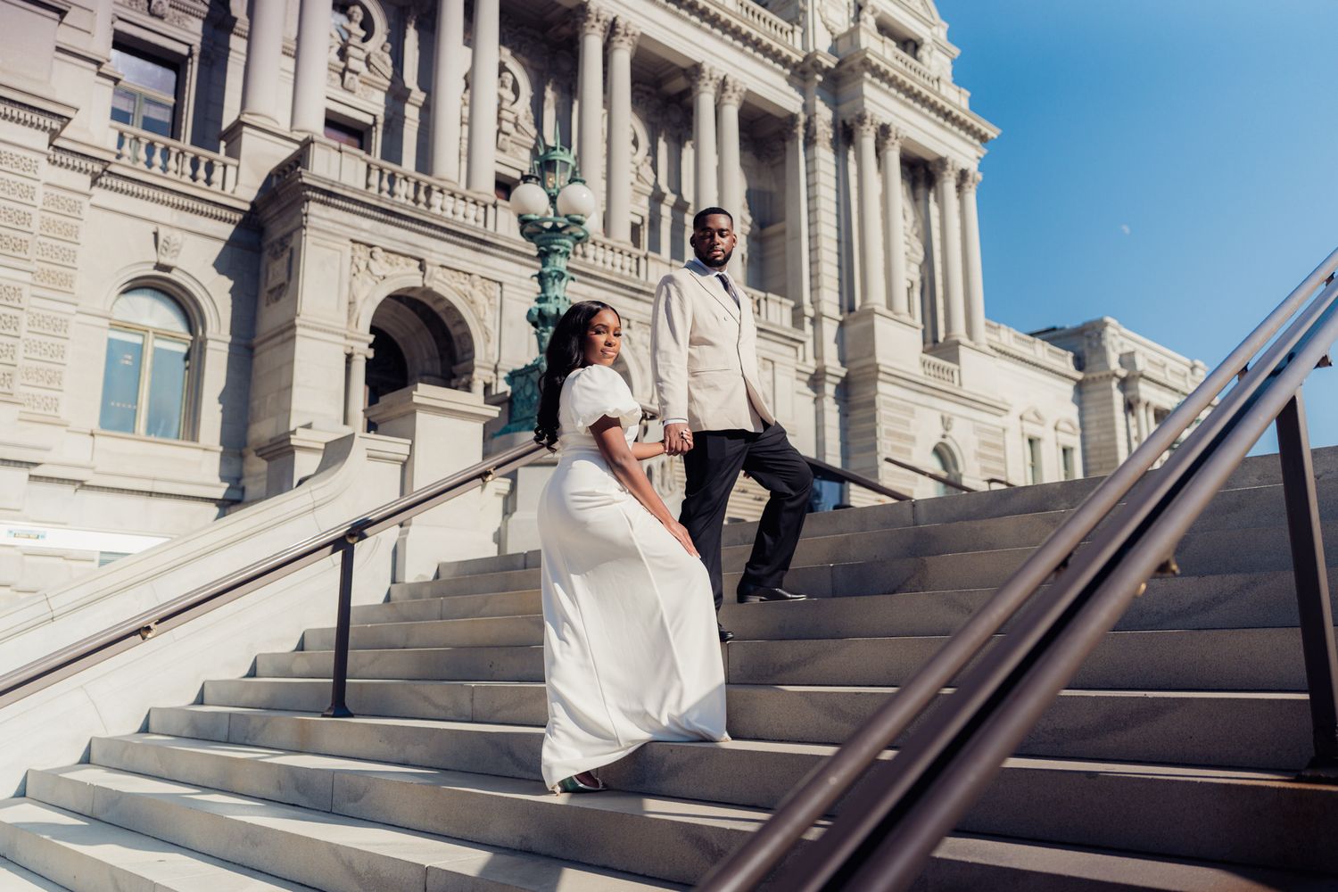 Couple in wedding attire descending grand stone steps outside a historic government building.