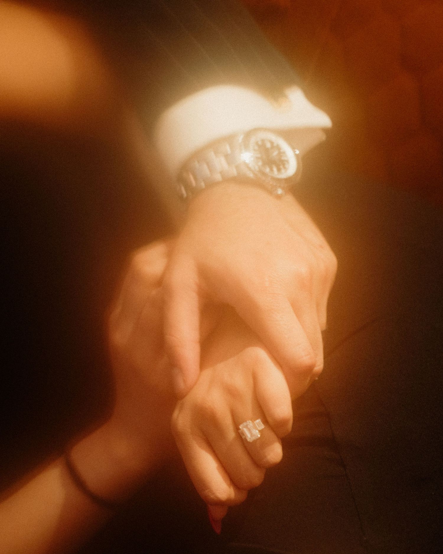 Close-up shot of hands with an engagement ring in warm ambient lighting.