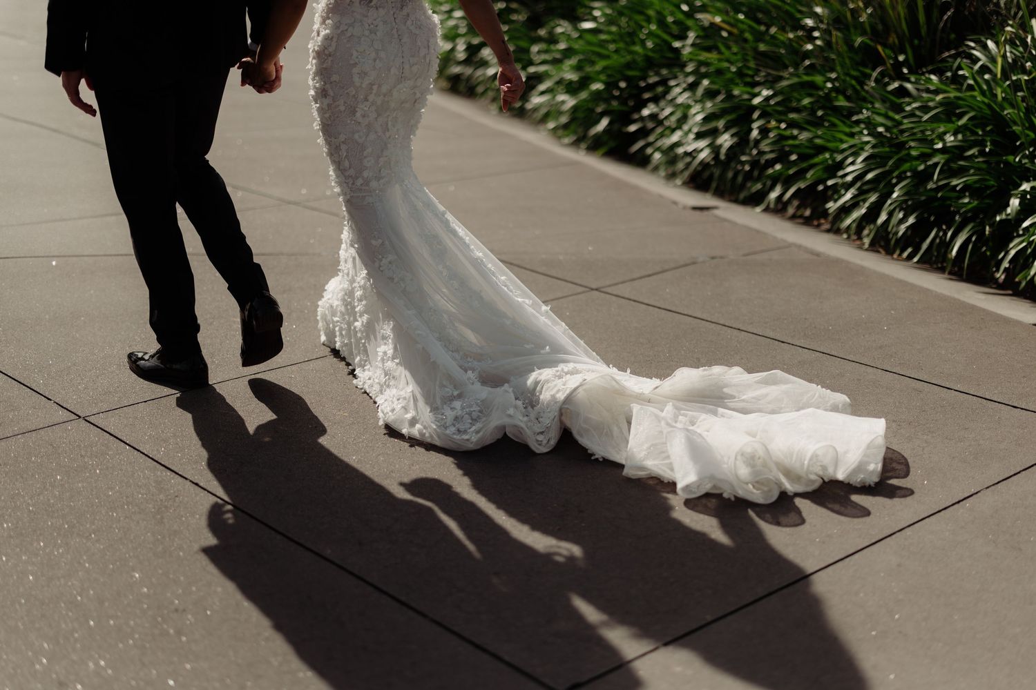 Flowing white wedding dress train and shadows on a concrete pathway.