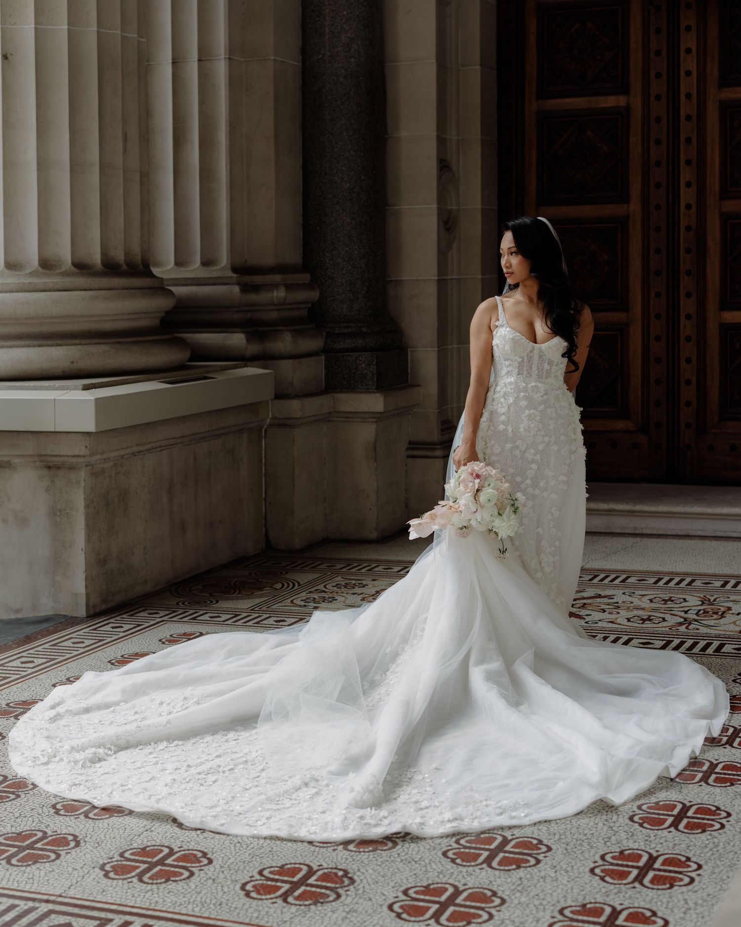 Elegant wedding dress with intricate lace details and long train against classic architectural columns.