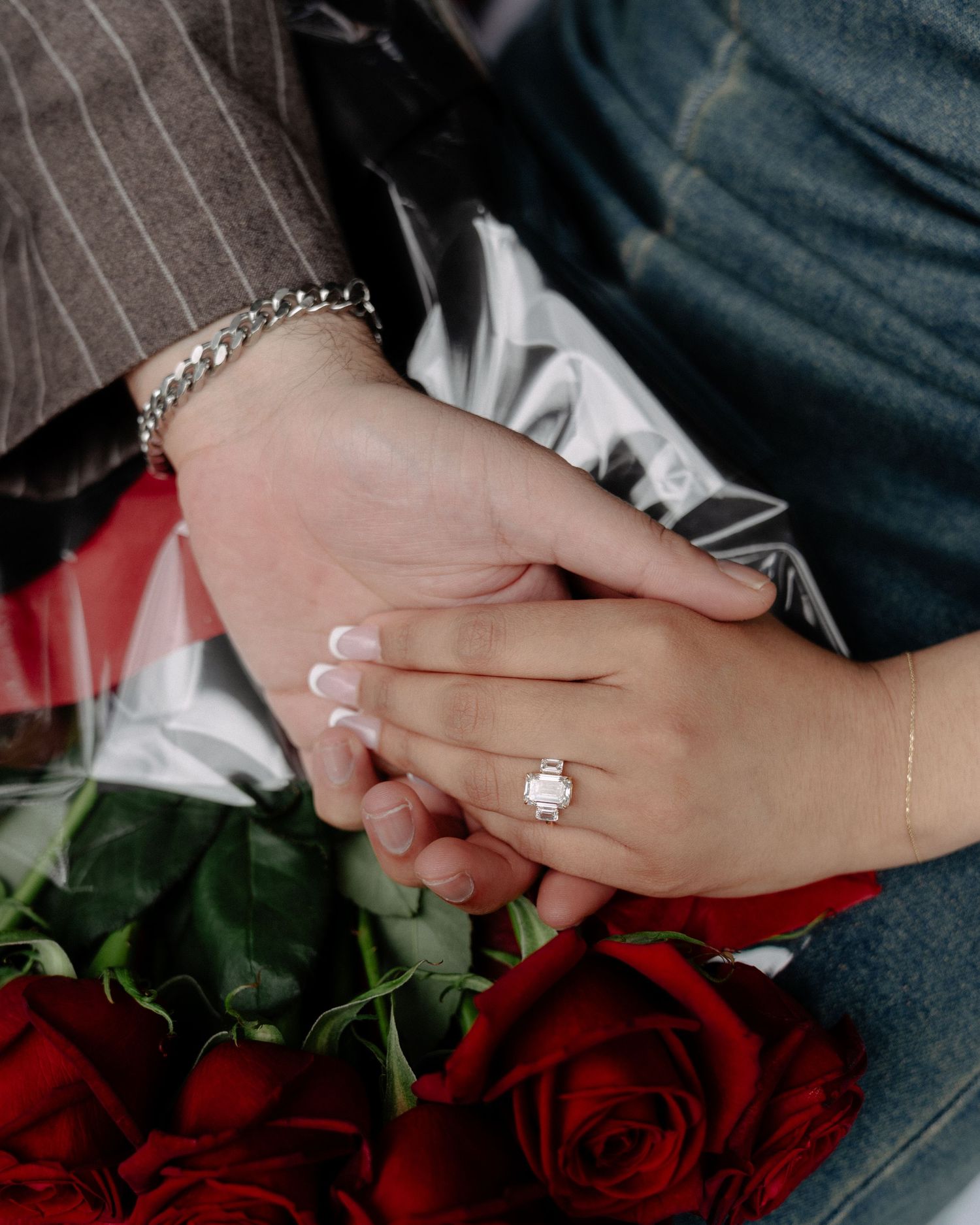 Close-up of hands with engagement ring and red roses showing romantic proposal moment.