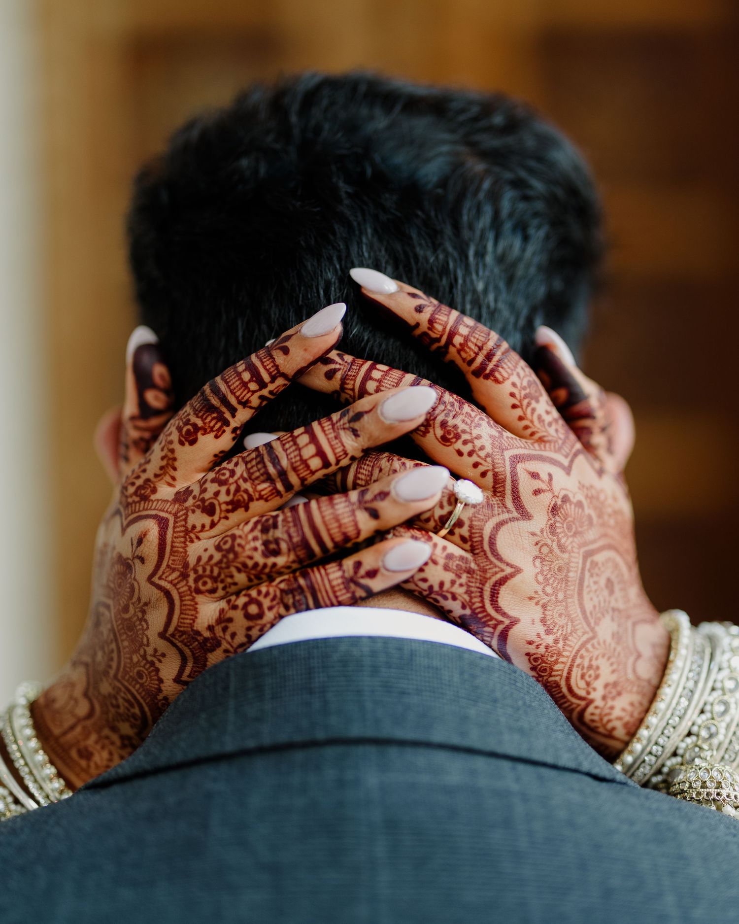 Bride with intricate henna mehndi designs on hands gently holding groom's neck at South Asian wedding.