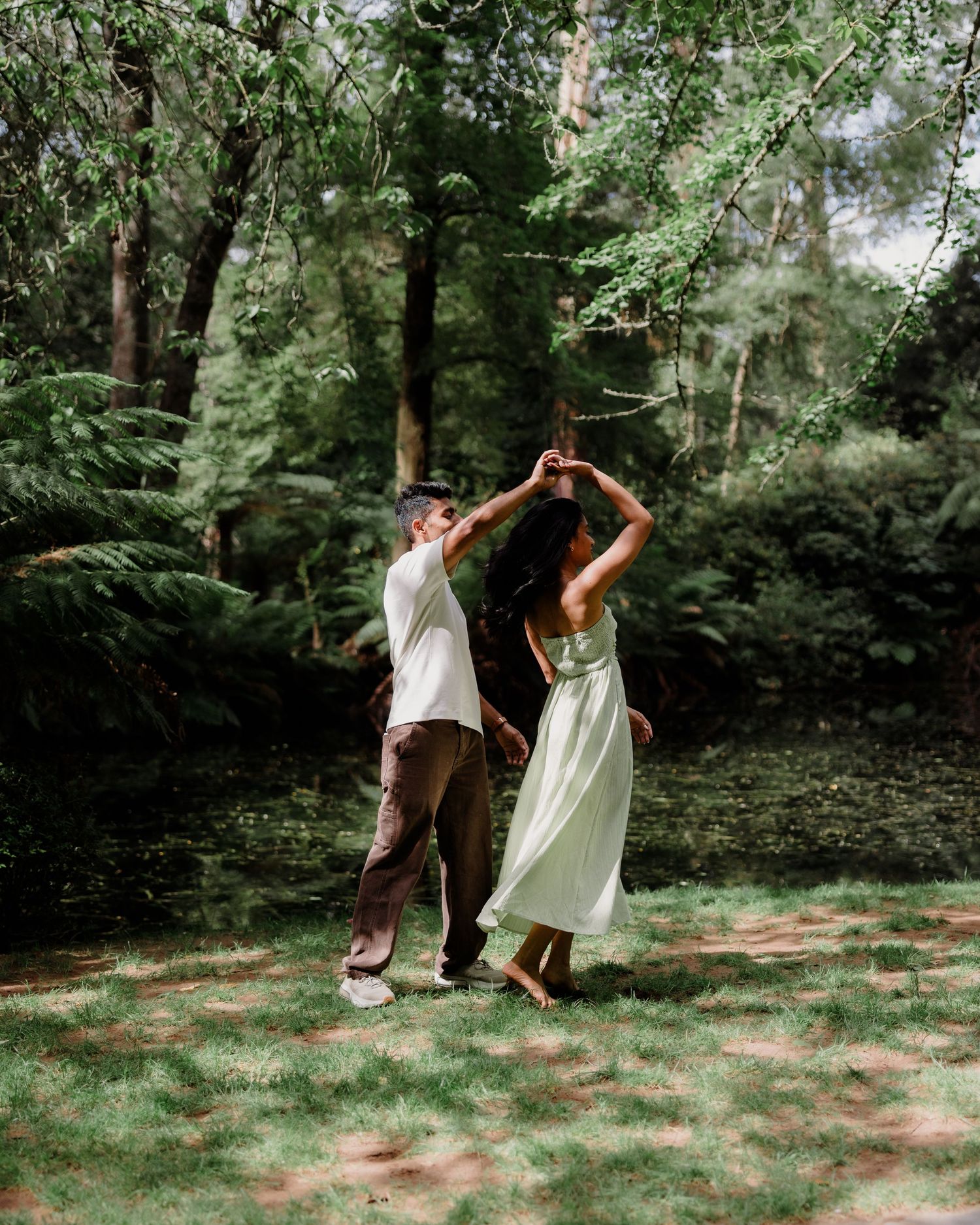 A couple dances together in a lush green forest, the woman in a flowing mint dress twirling gracefully.