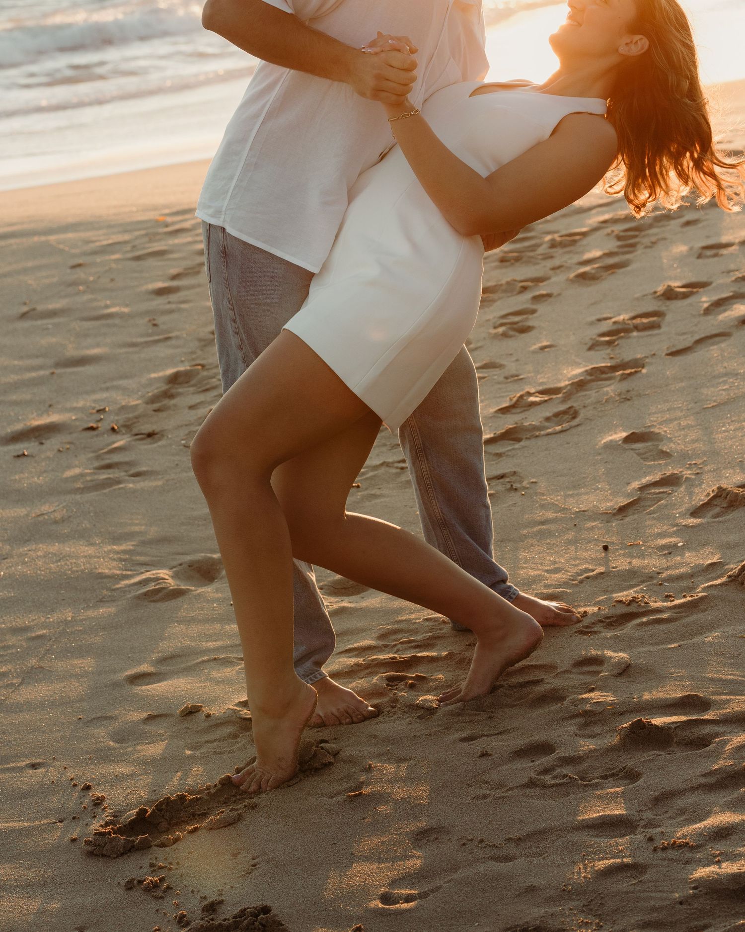 Couple dancing barefoot on beach at sunset.