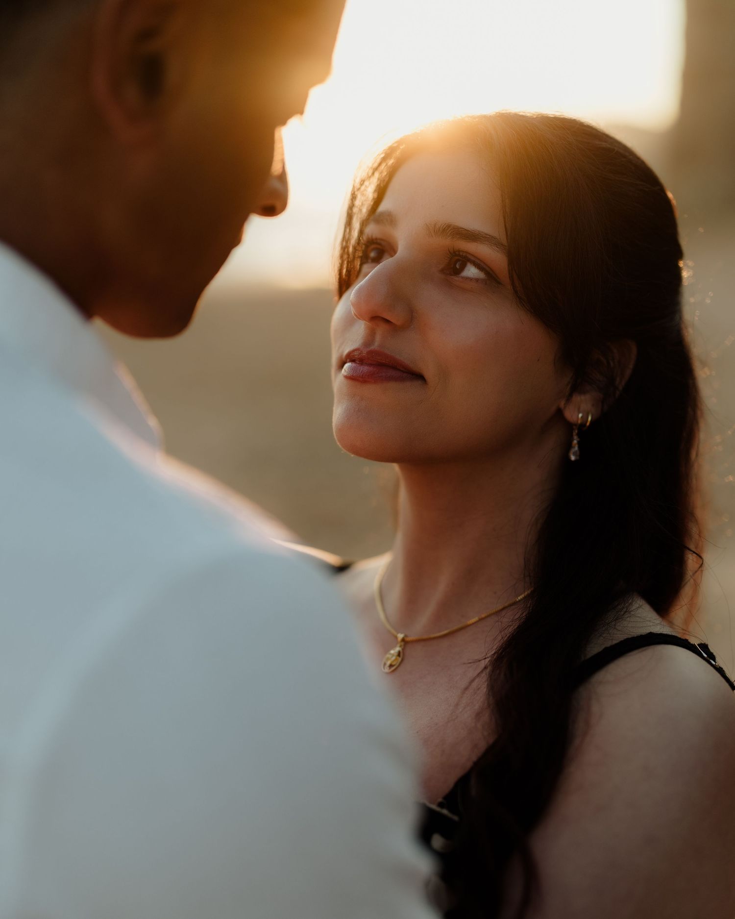 A woman gazes lovingly at a man during a golden hour couples portrait session outdoors.