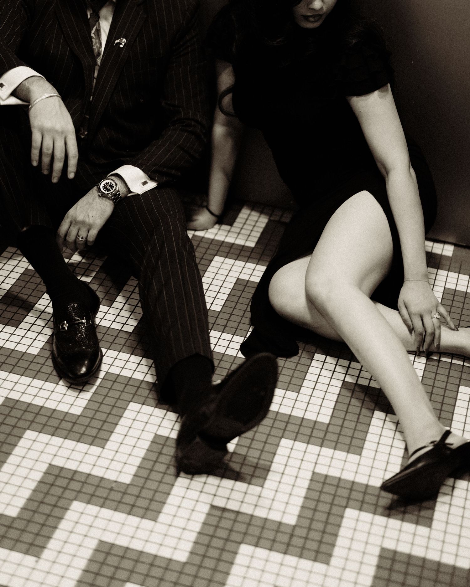 Black and white photo of feet and legs on a tiled floor.