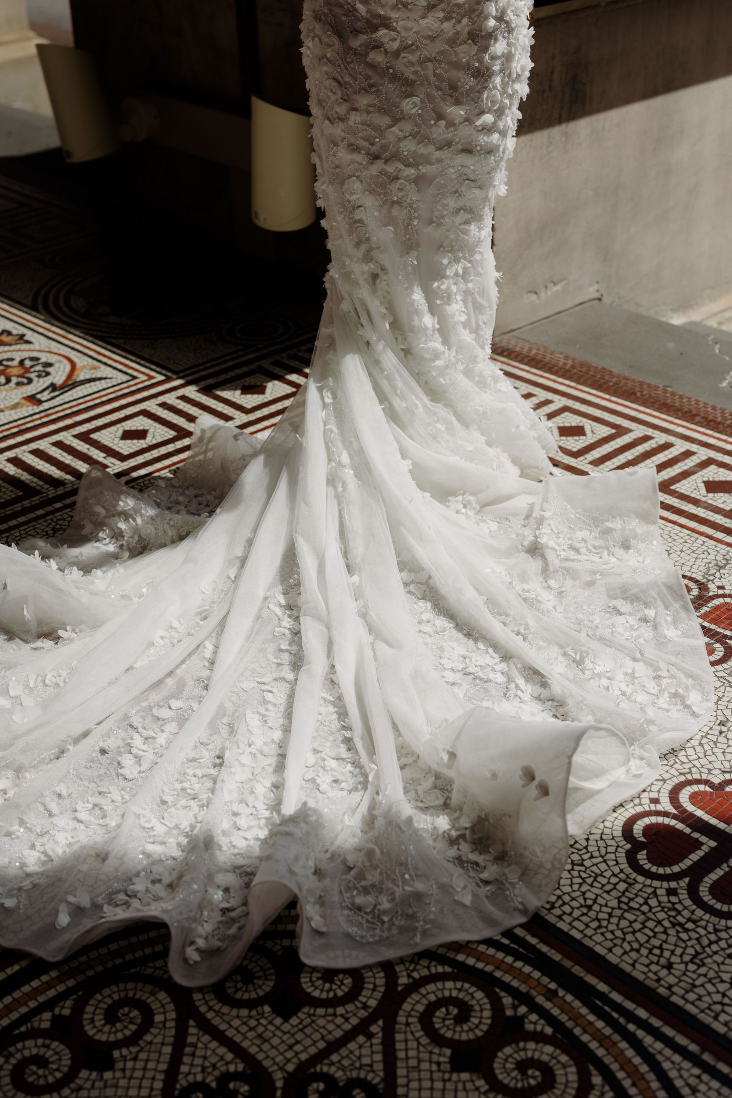 Close-up detail of an ornate white wedding dress train with lace patterns on decorative floor tiles.