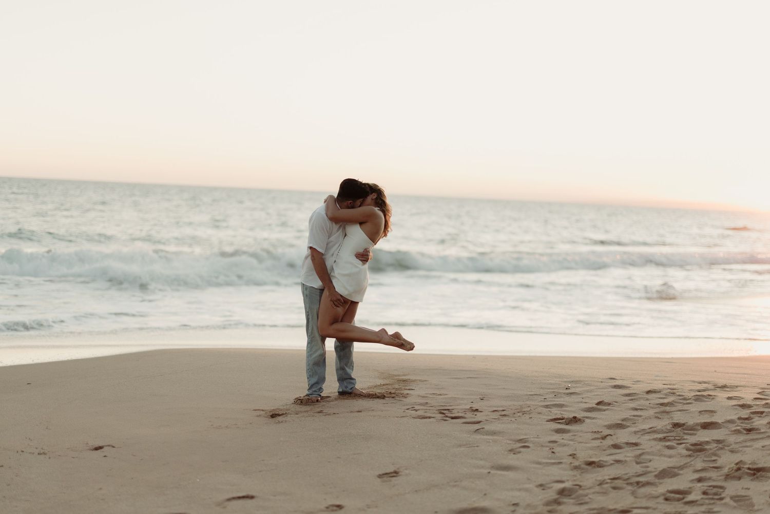 Romantic sunset beach scene with couple silhouetted against ocean backdrop.