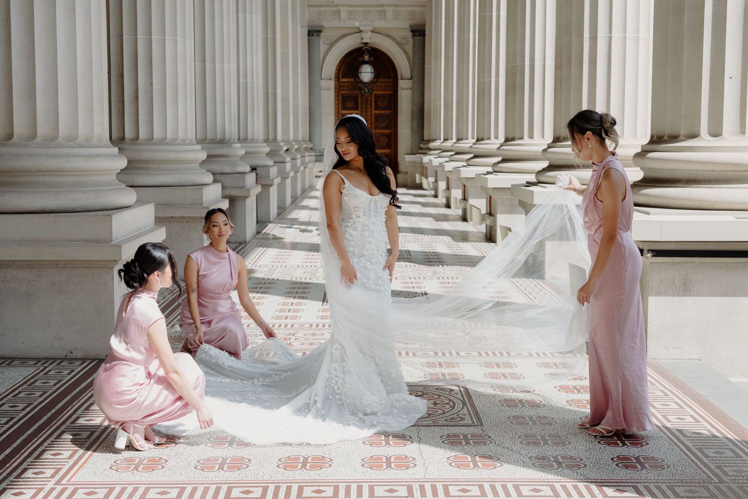 Elegant bridal party posing between classical white columns in formal attire.