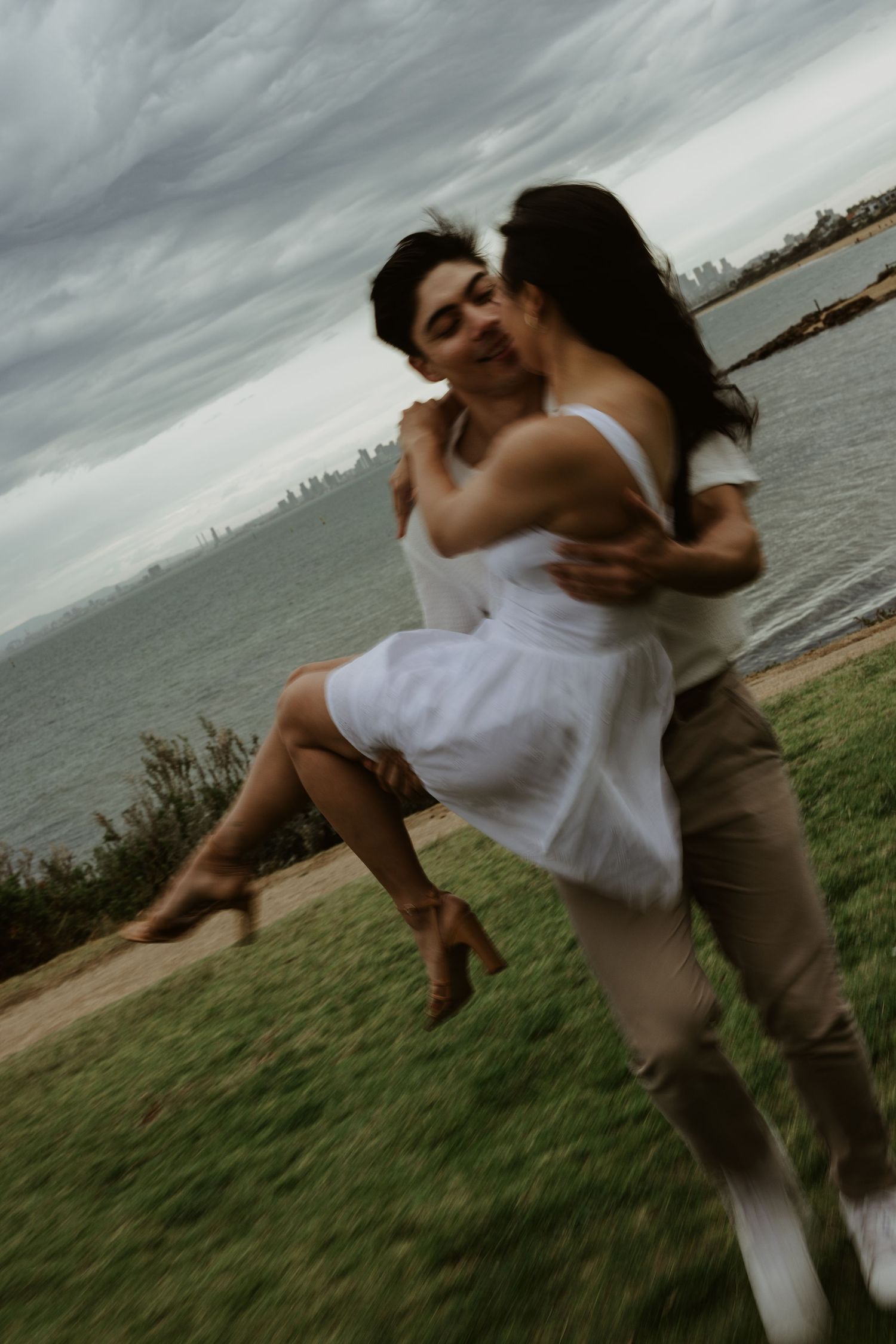 Couple performs romantic dance moves on a coastal cliff with dramatic cloudy sky.