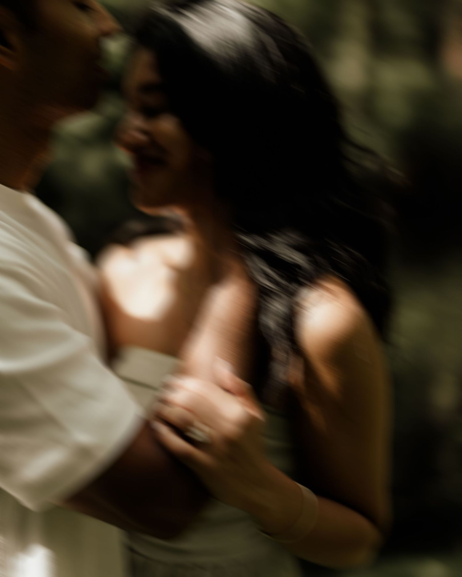 A couple shares a joyful, blurred motion moment embracing outdoors, captured in soft natural light.