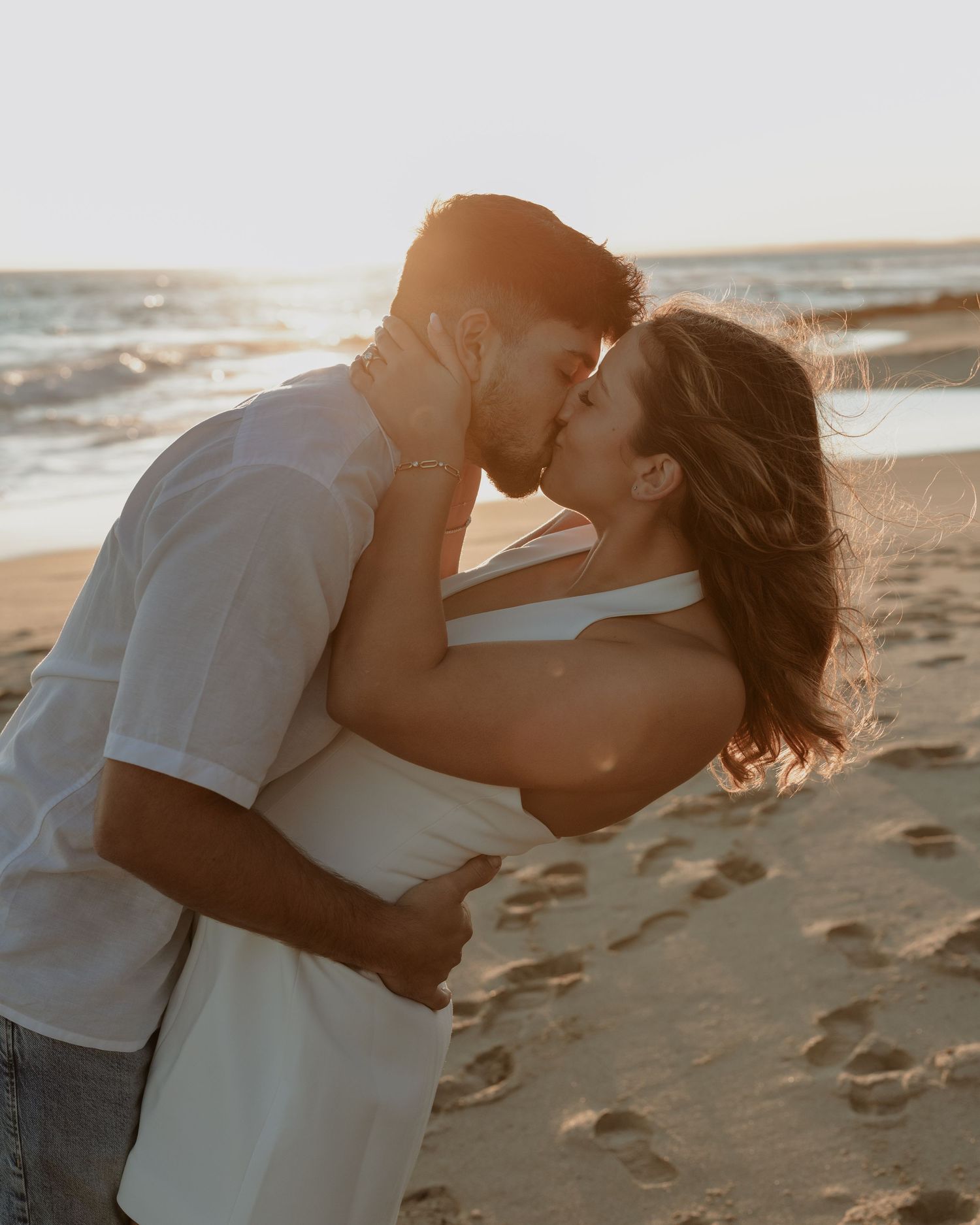 Intimate beach photoshoot captures a couple in white clothing during sunset.