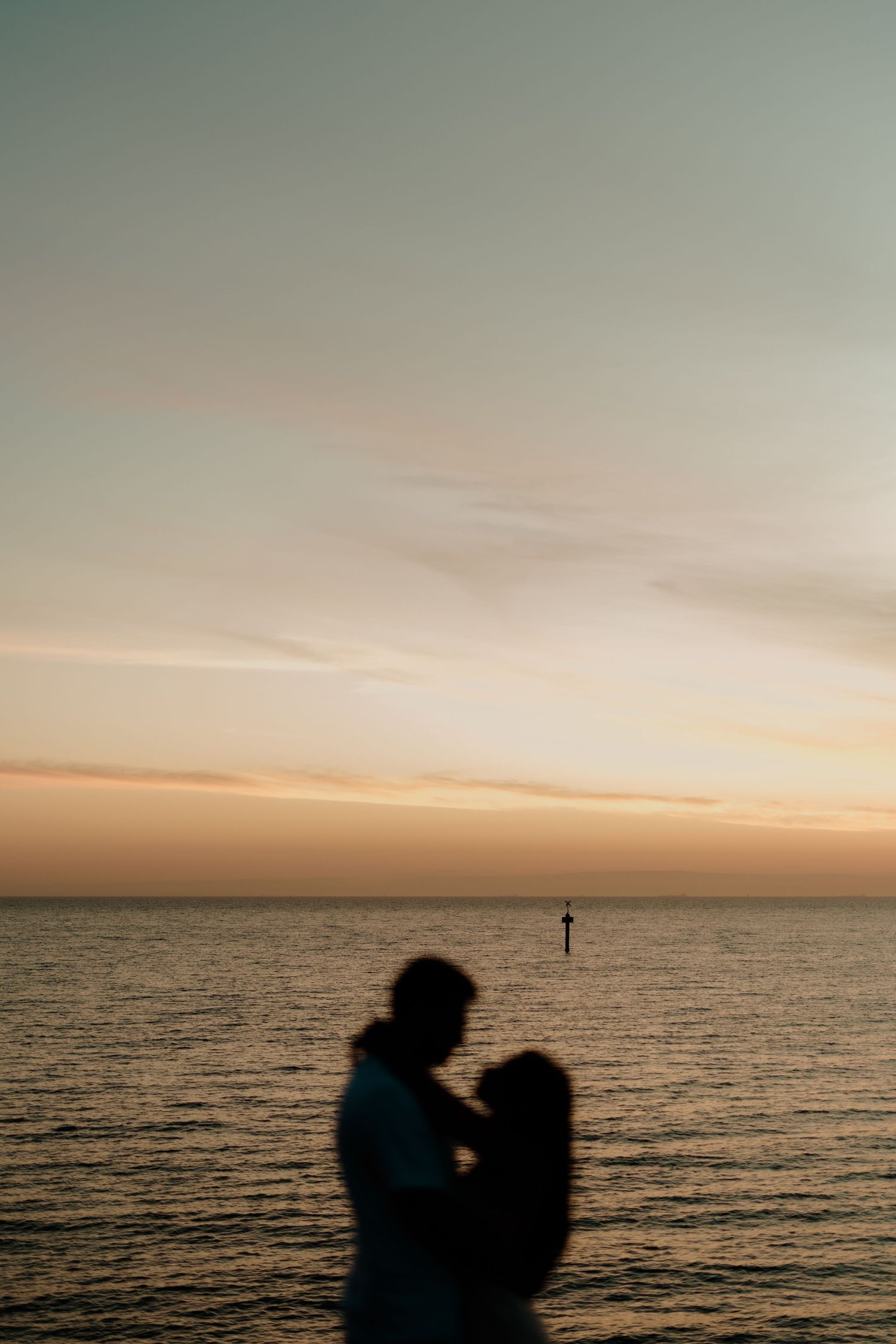 Silhouette of a romantic couple embracing at sunset over a calm ocean with a warm golden sky.