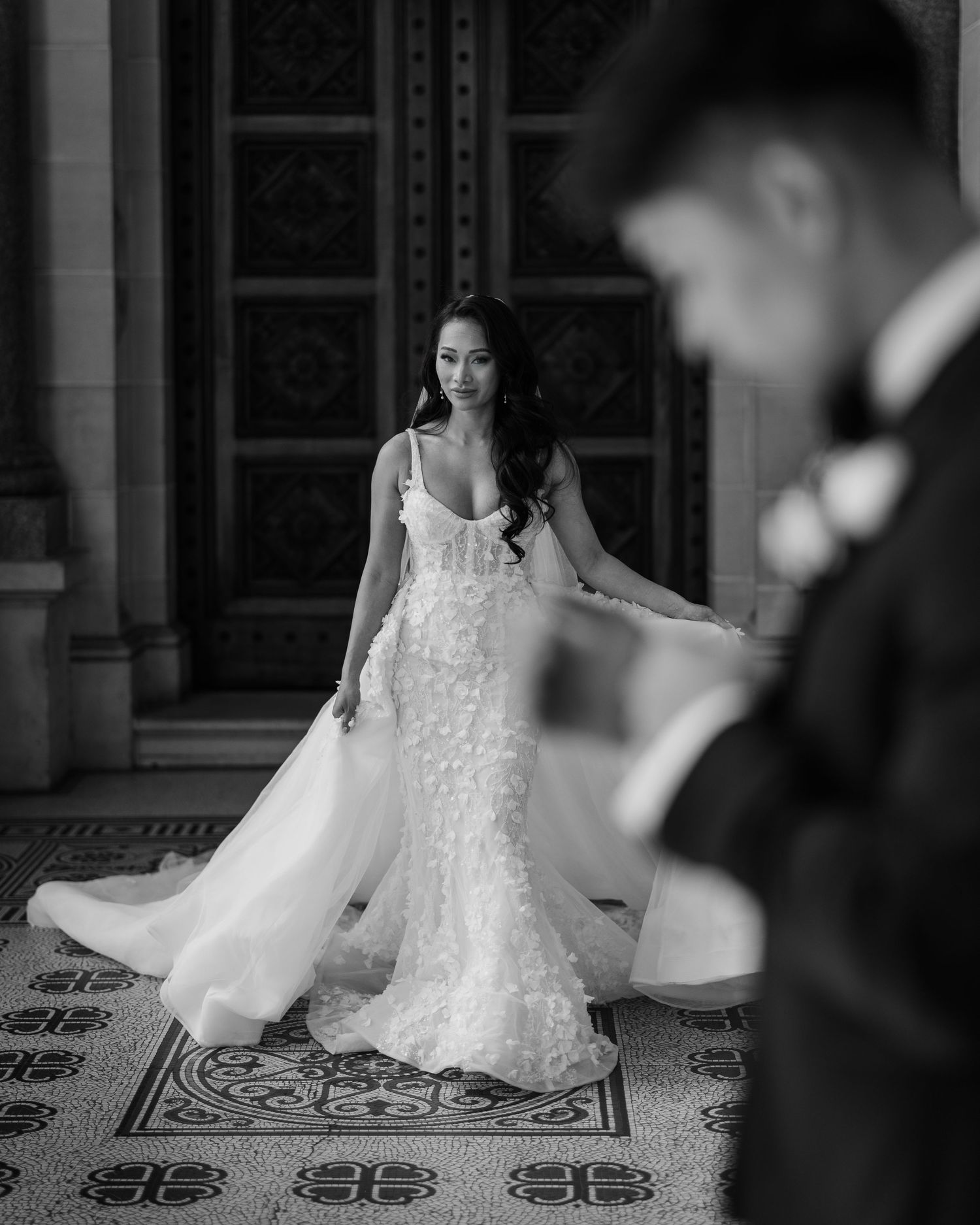Stunning lace wedding gown photographed in black and white against ornate architectural backdrop.