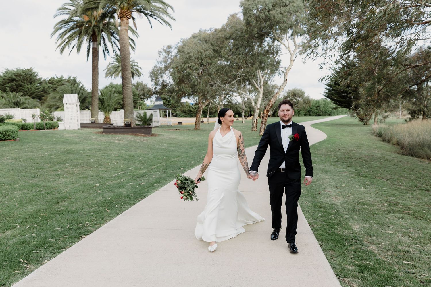 Wedding couple walking along a palm-lined path outdoors.