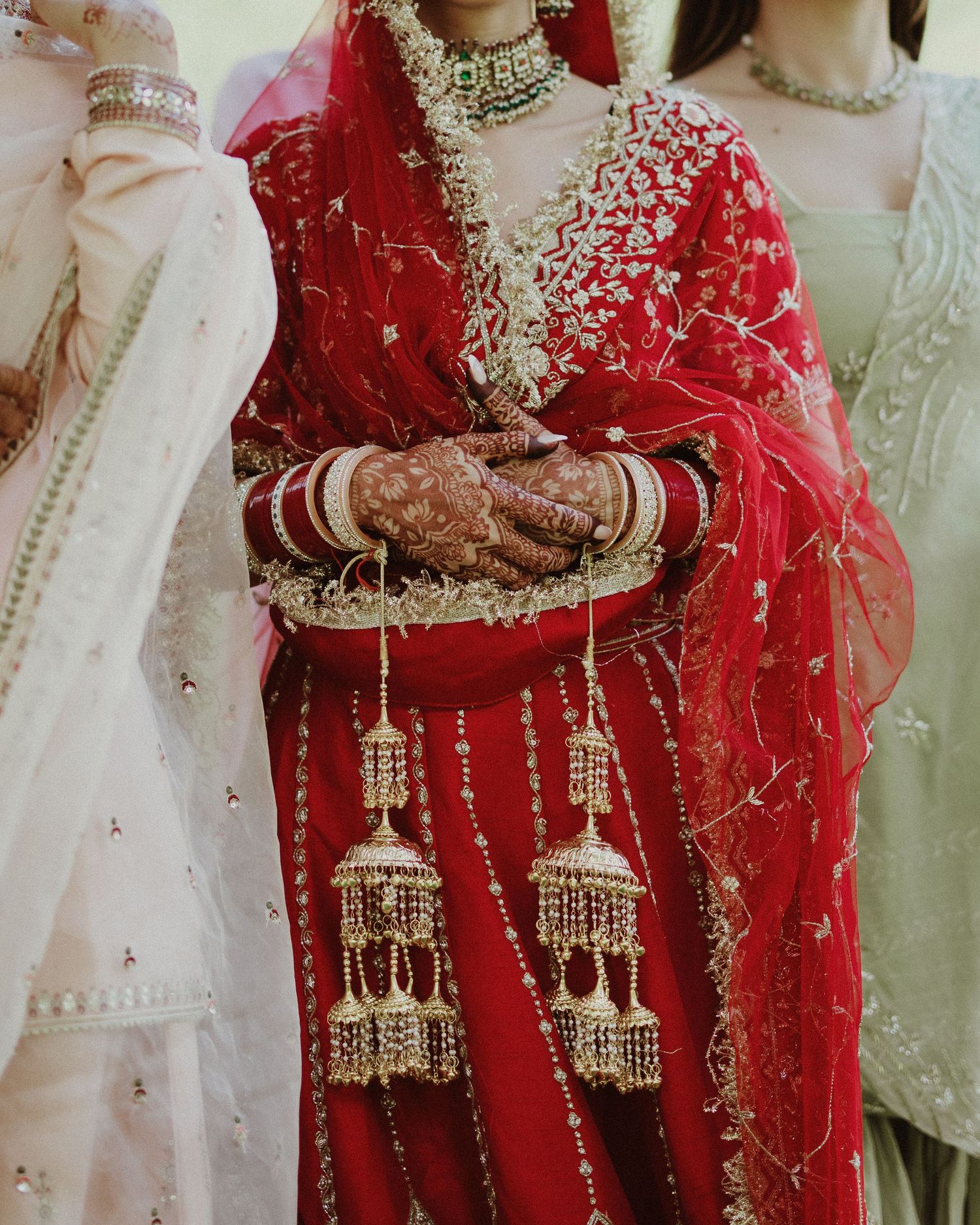 Close-up detail of traditional Indian bridal jewelry and red wedding attire with intricate gold embellishments.