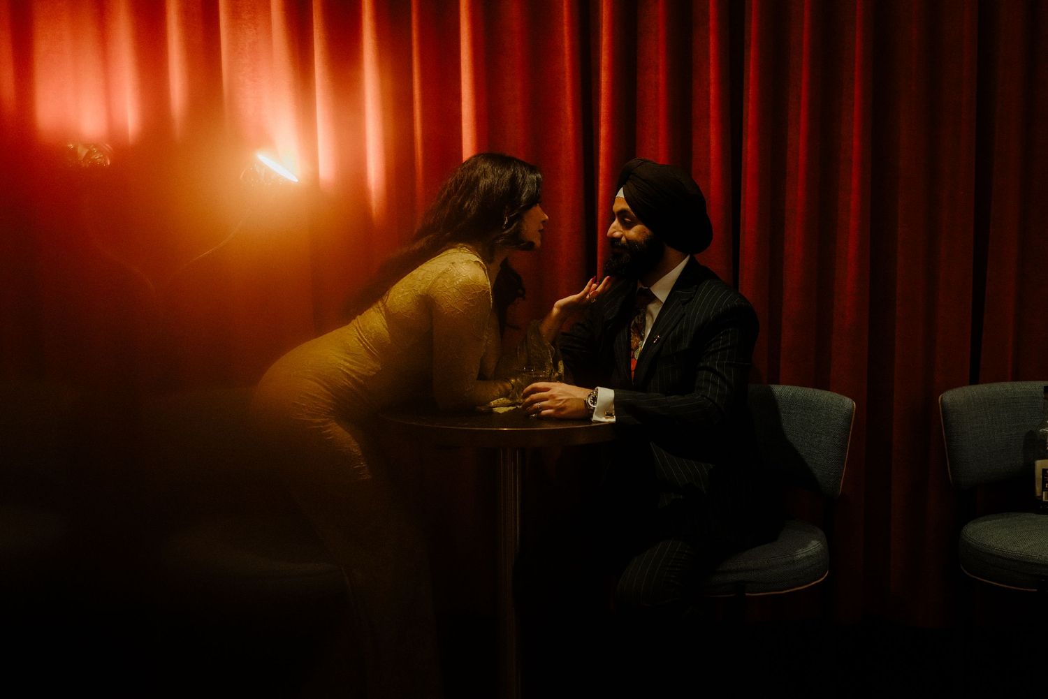 Romantic couple sharing an intimate moment in a dimly lit restaurant with red curtains.