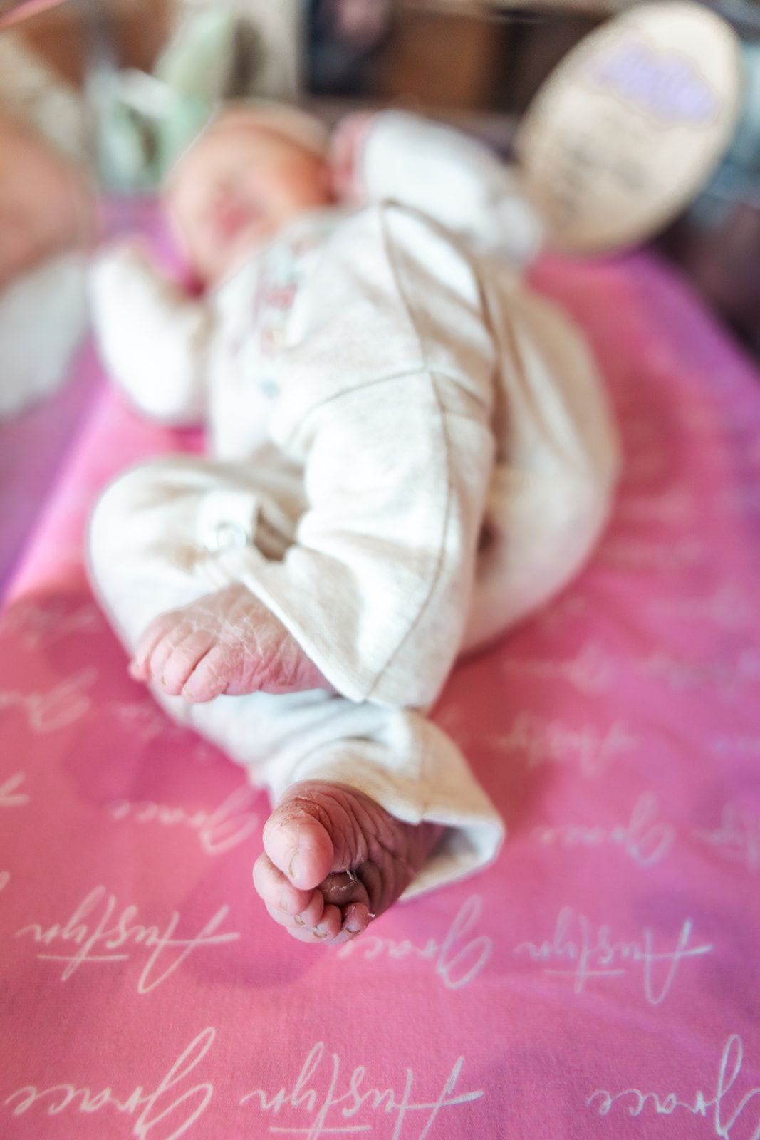 Close-up of newborn's tiny feet in white clothing on pink patterned fabric. fresh 48 hospital session
