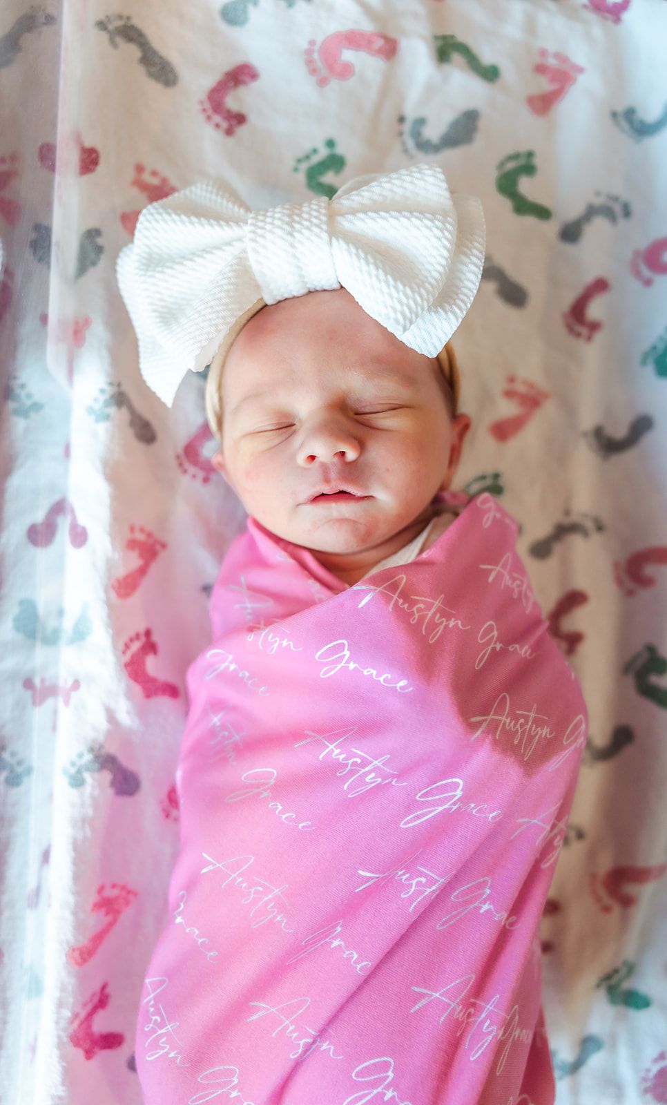 Sleeping newborn wrapped in pink swaddle wearing large white bow. fresh 48