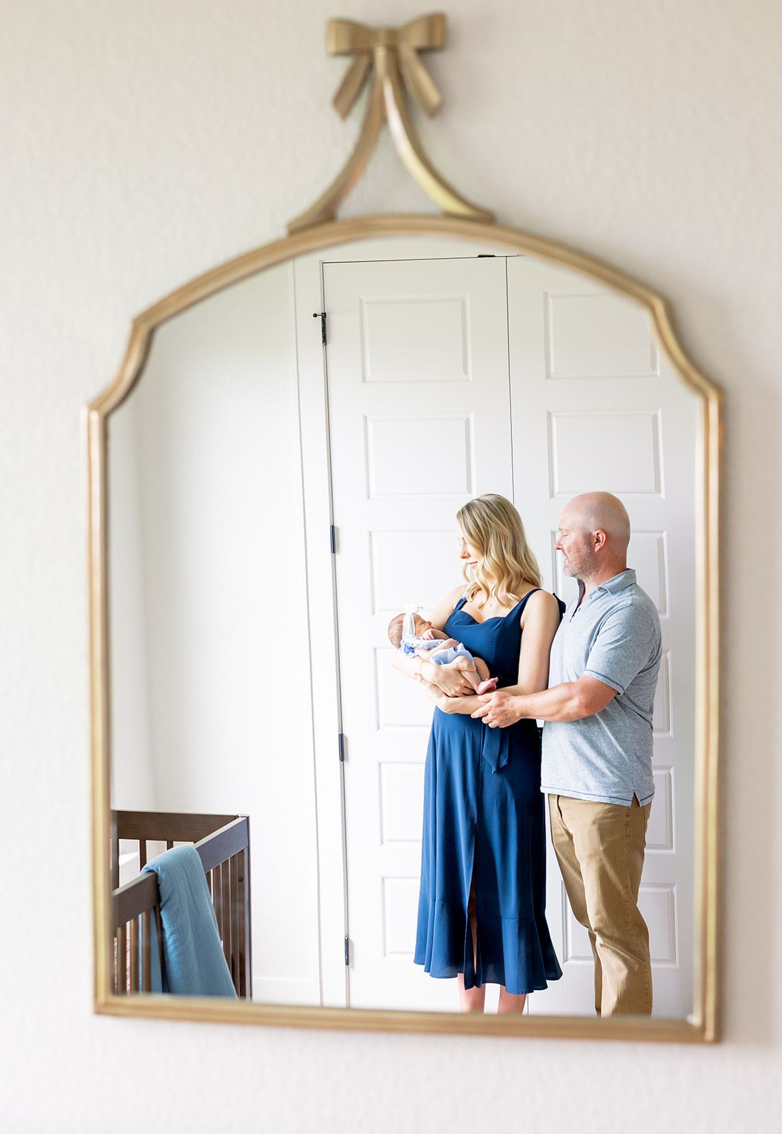 A gold-framed mirror on a white wall showing reflections of a couple admiring newborn together. fresh 48 session