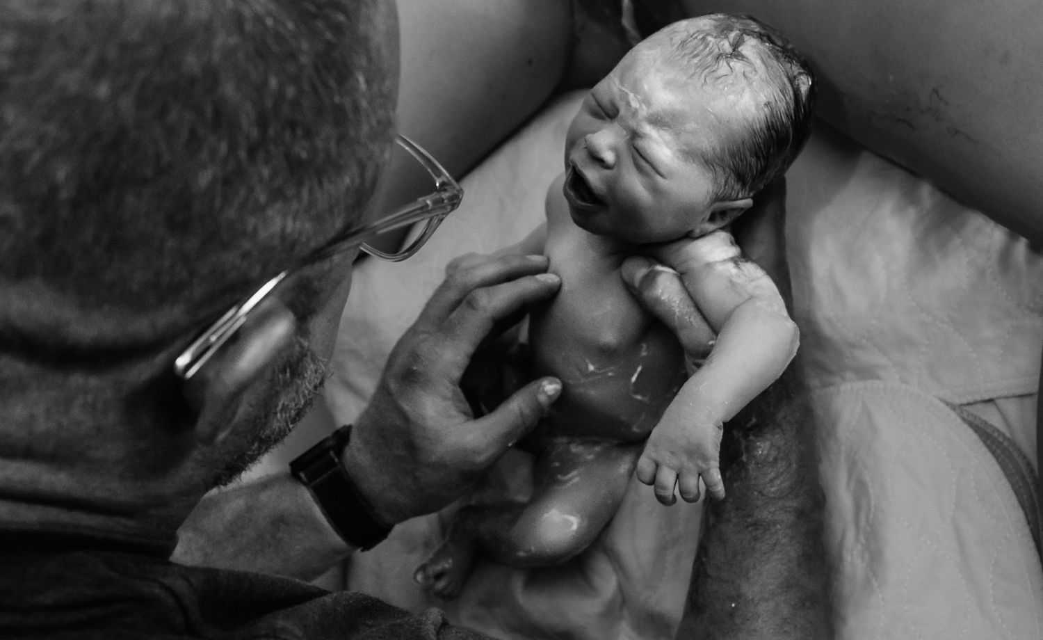 Dad catching his own baby after his wife gave birth vaginally and unmedicated in a hospital bed