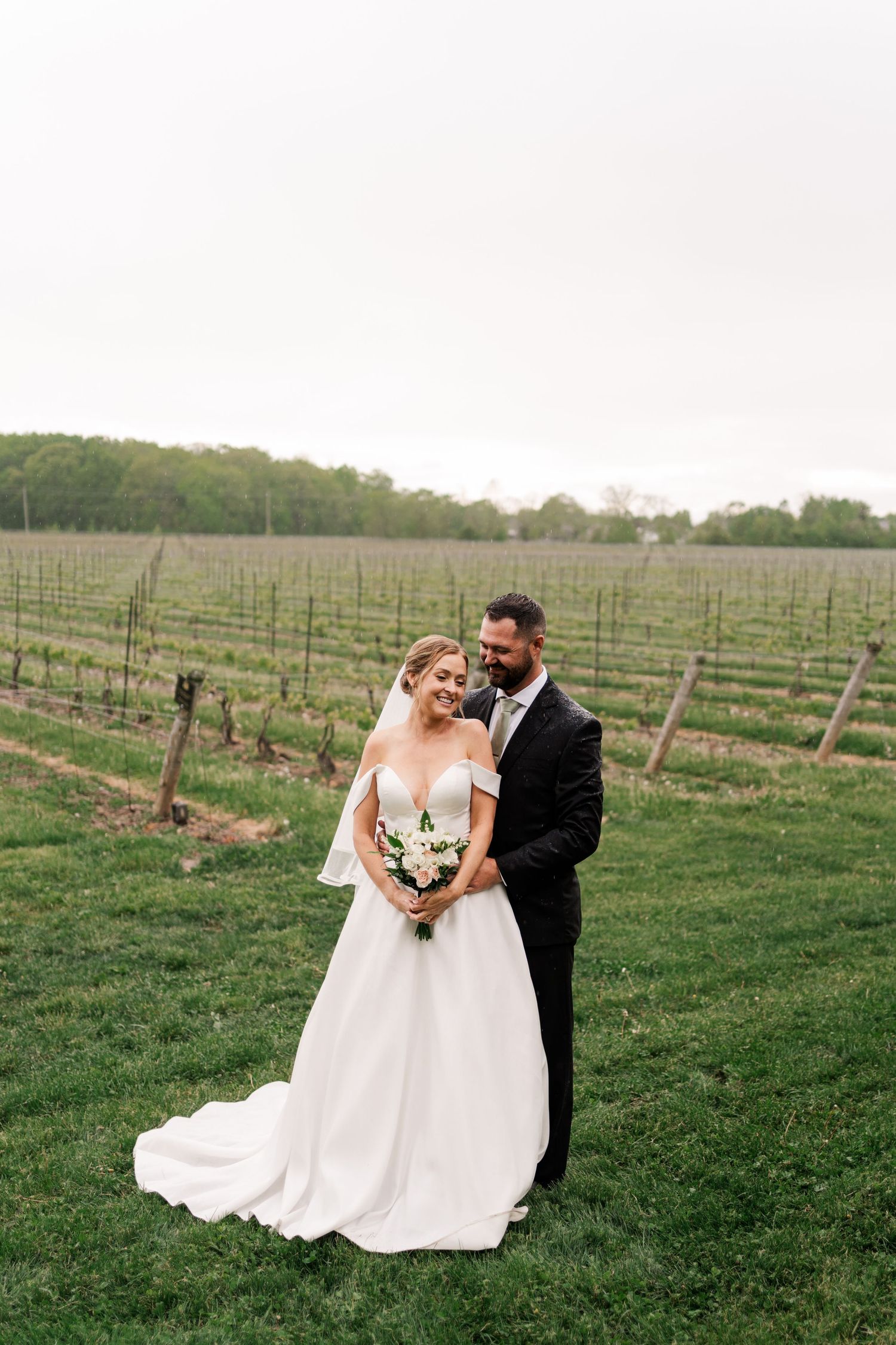 Newlywed couple poses together in a scenic vineyard with rows of grapevines on an overcast day.
Niagara wedding photos.