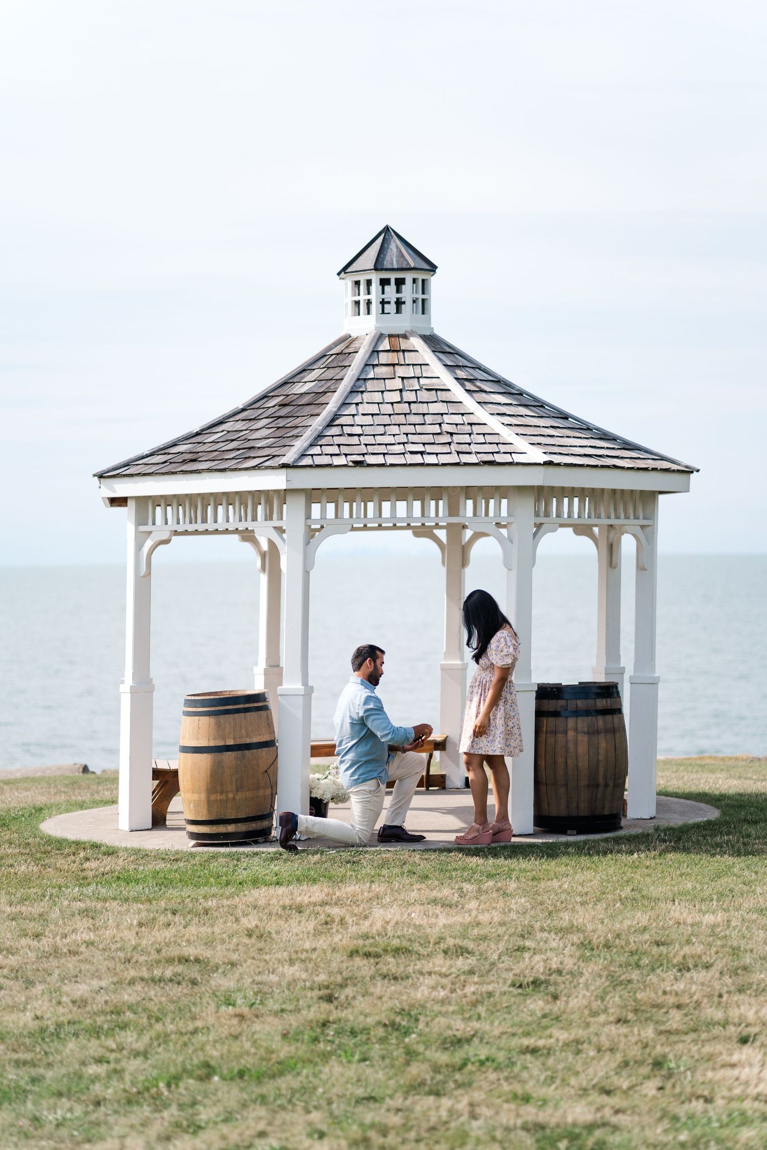 White wooden gazebo overlooking the ocean with decorative wine barrels on a grassy hill.
Niagara proposal photos