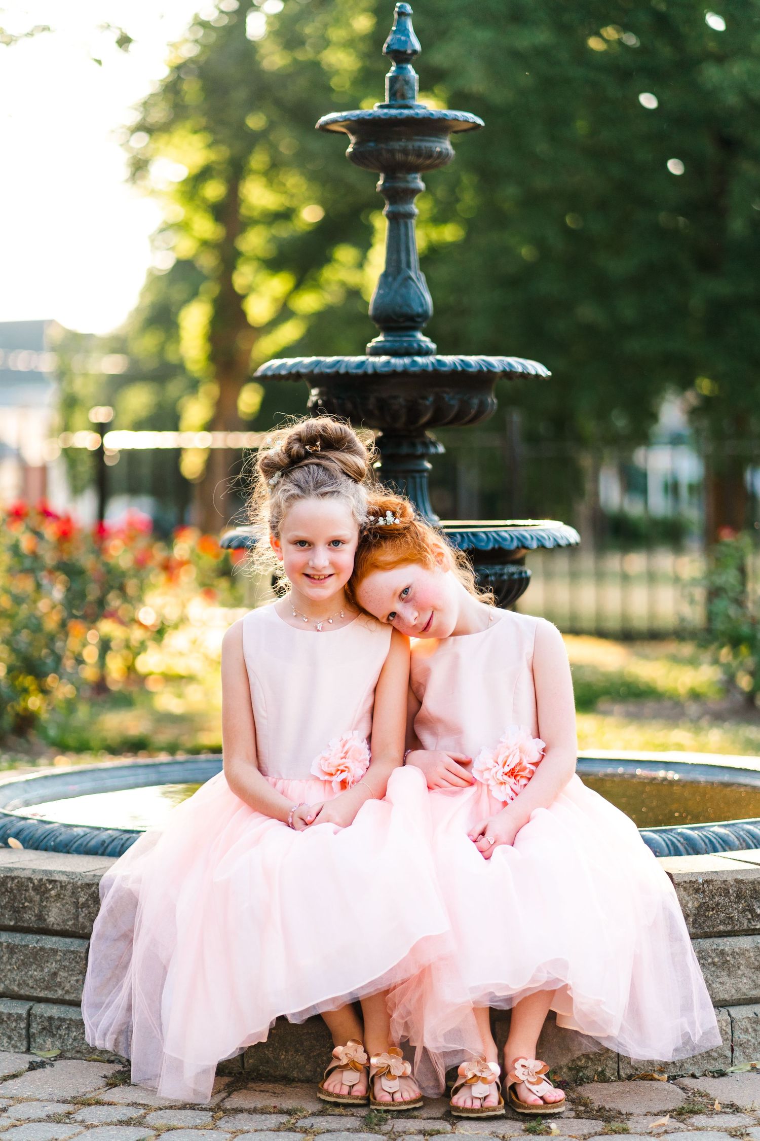 Two young girls in pink tulle dresses sit together on a decorative stone fountain.
Family photos in Niagara