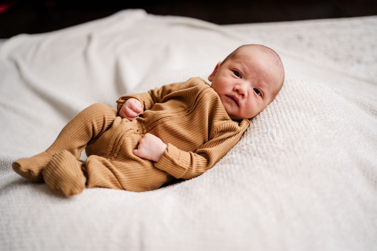 Baby wearing brown outfit resting on soft white textured surface.
Niagara newborn photos.