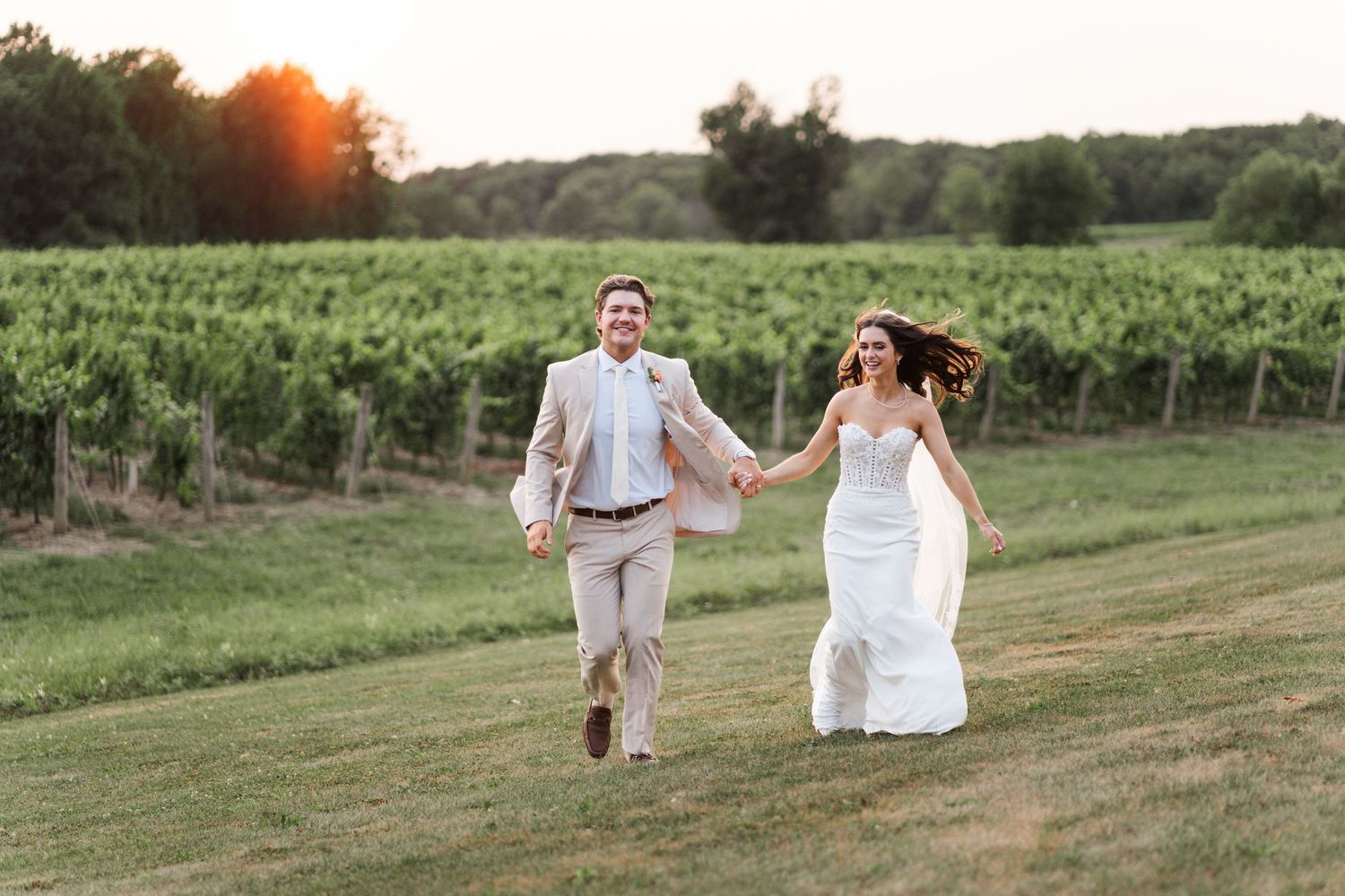 Couple runs hand-in-hand through vineyard at sunset.
Niagara wedding photos.