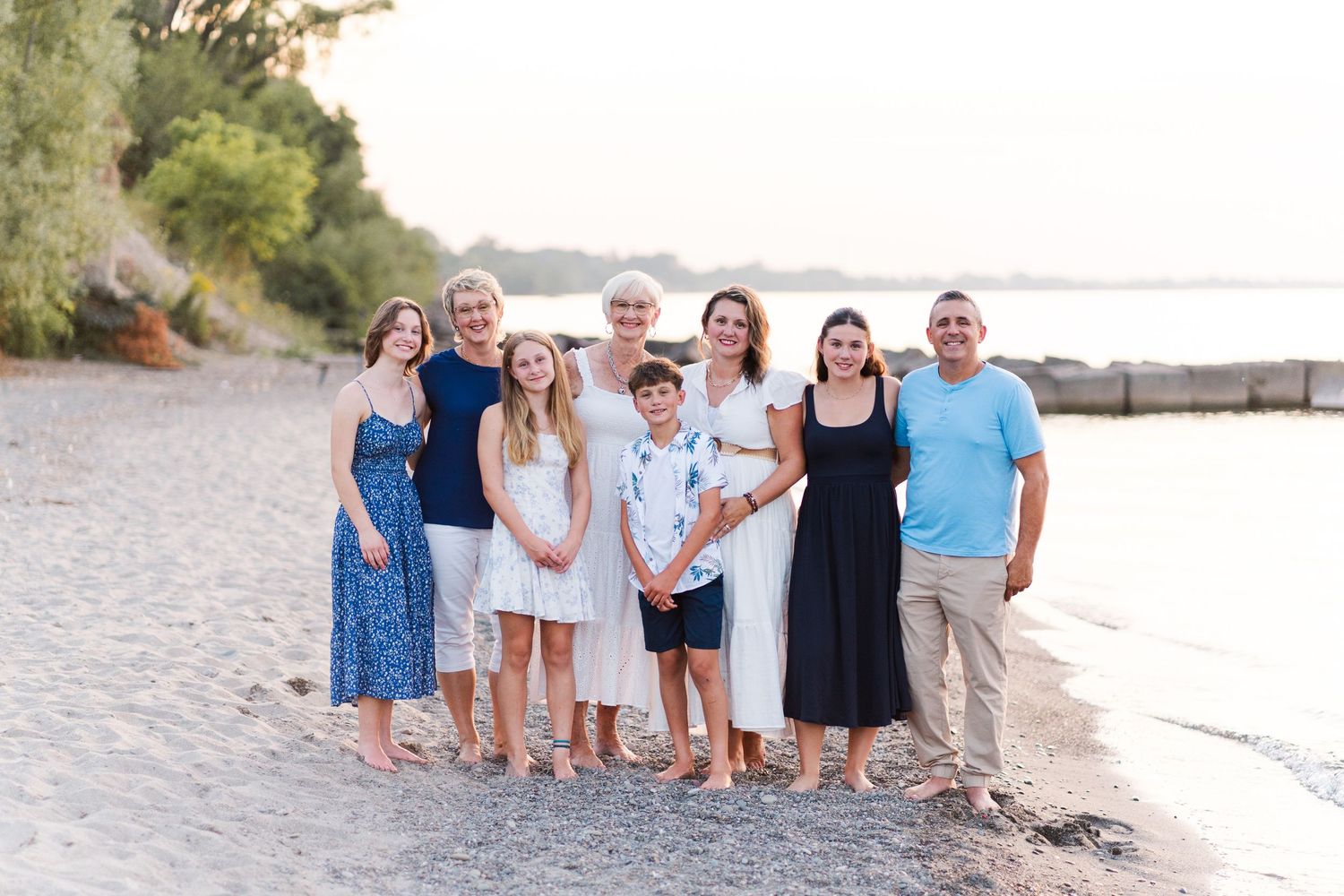 Group standing together on a sandy beach at sunset with water and trees in the background.
Niagara family photos.
