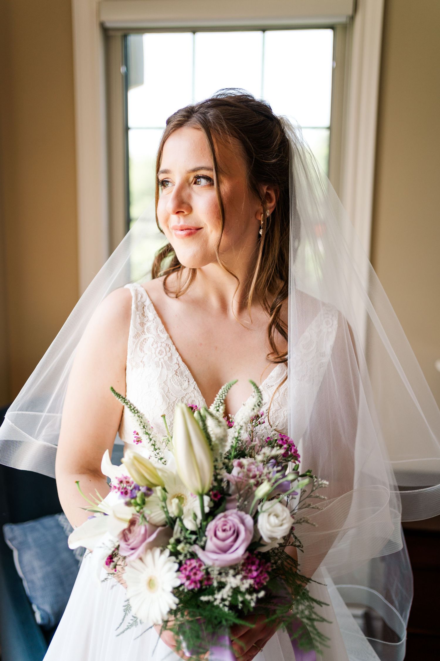 Bride in white wedding dress holds elegant bouquet of lilies and purple flowers by window.
Niagara Wedding photography.