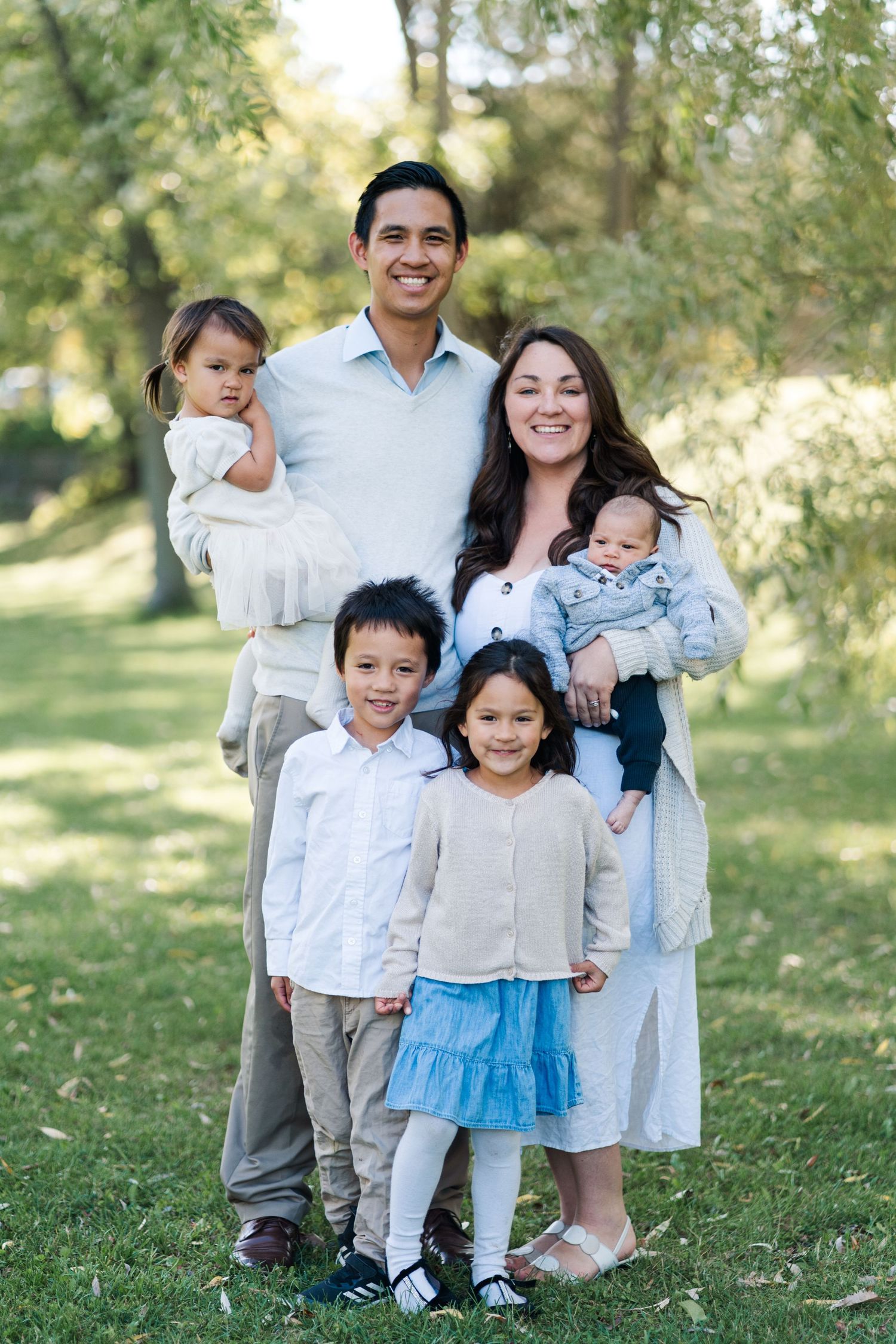 Family portrait of six members in coordinated outfits standing together on grass under trees.
Niagara family photos.