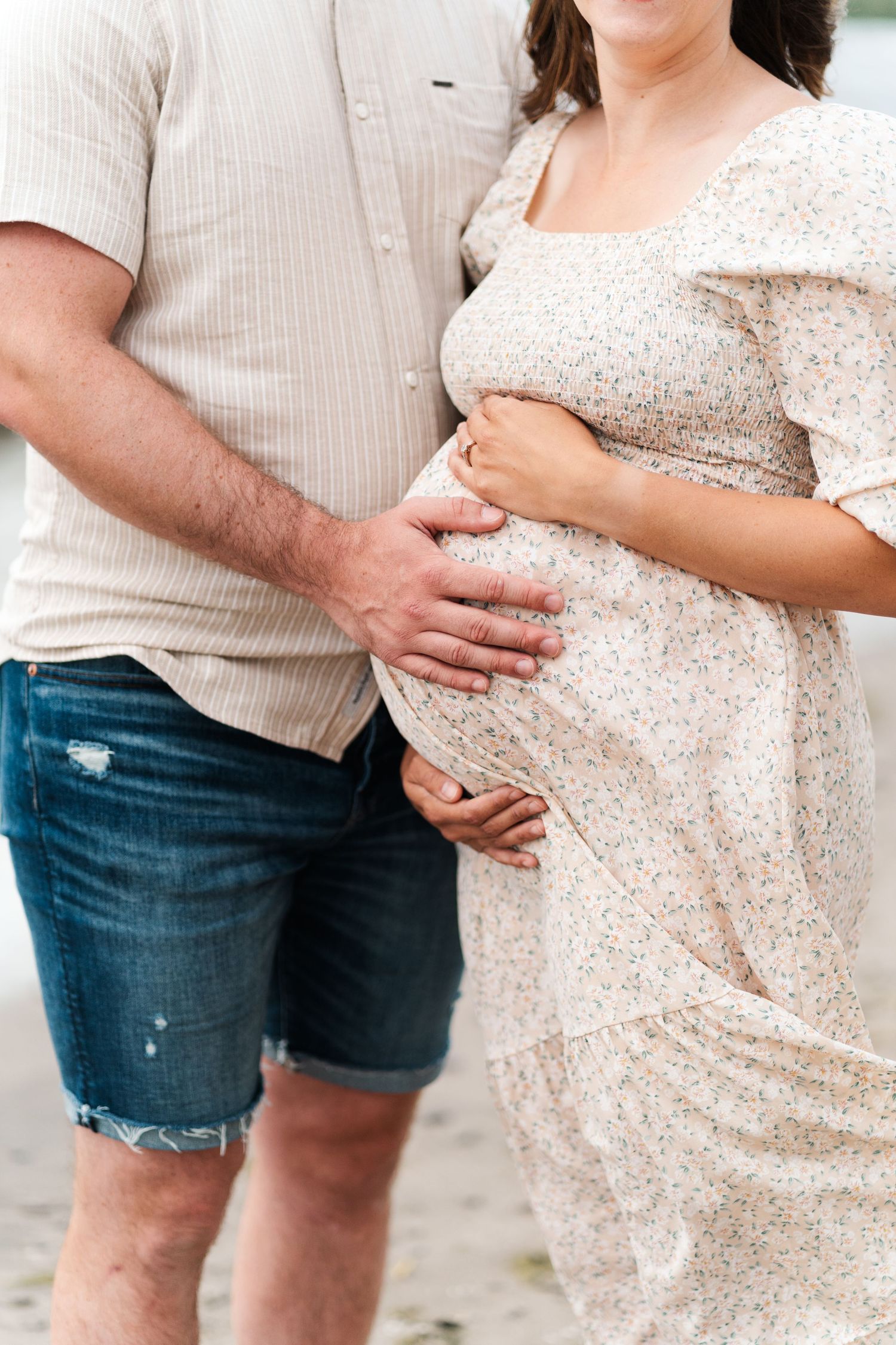 Close-up of couple's hands cradling a pregnant belly in a floral dress.
Niagara maternity photos.