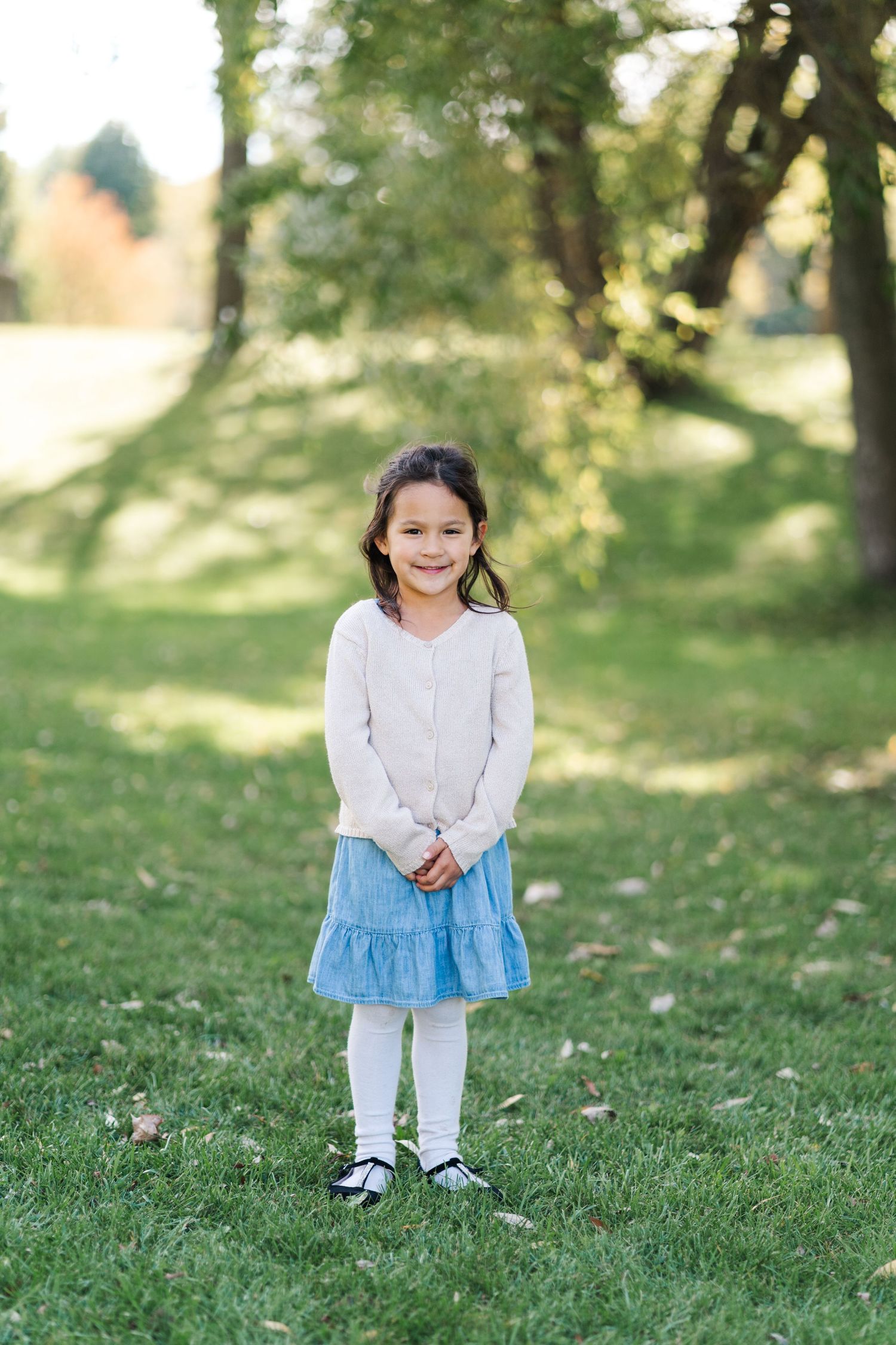 Young child wearing a white sweater and blue skirt stands on grass in a park setting.
Niagara family photos.