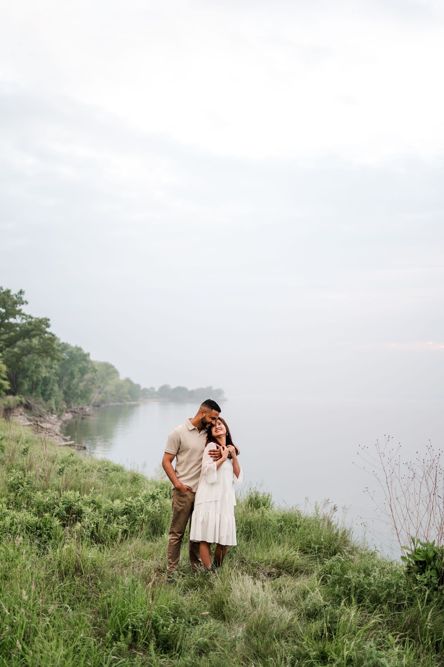 Couple embraces on a grassy hillside overlooking a misty lake during a romantic photoshoot.
Niagara engagement photos.