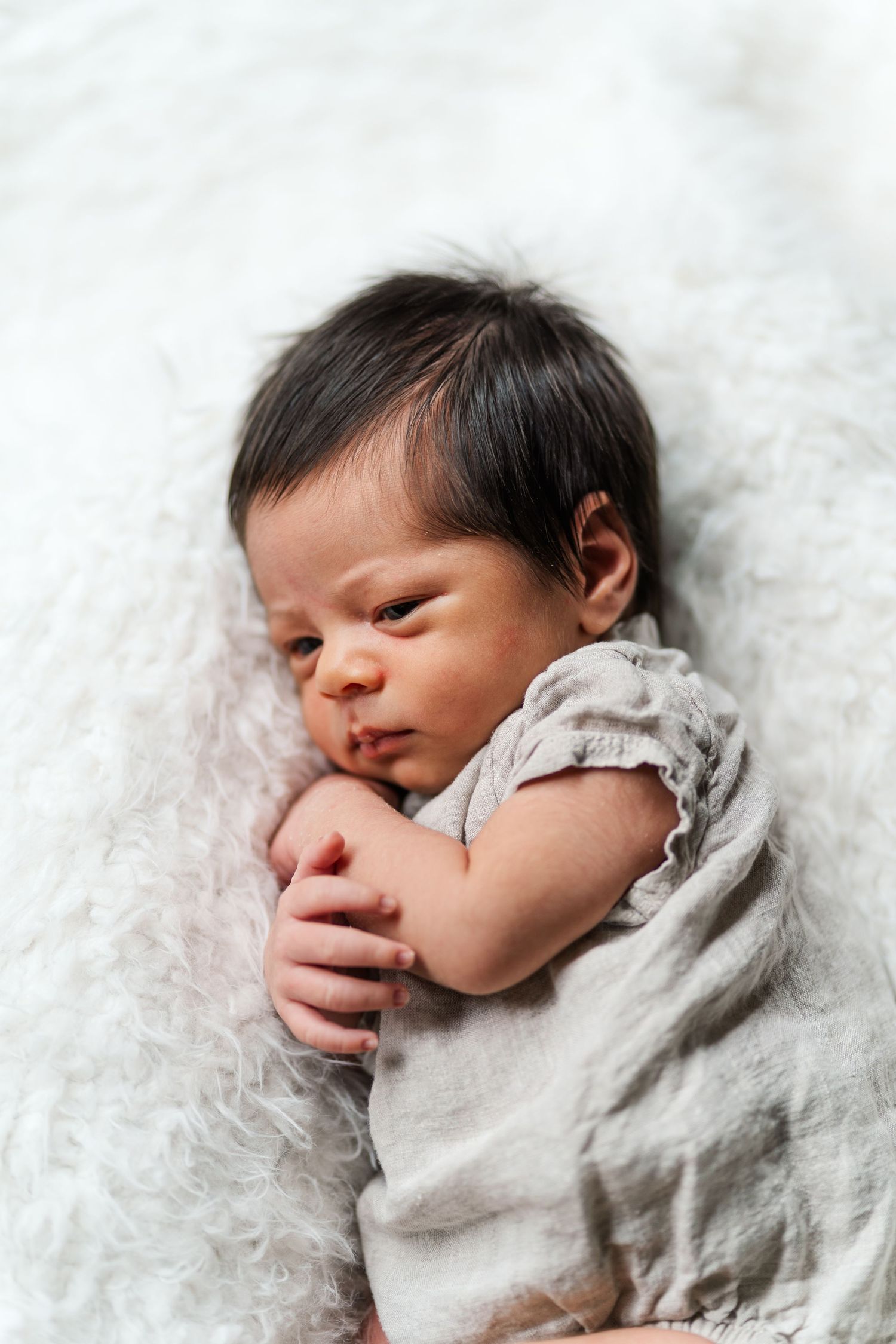 Newborn wrapped in light gray swaddle on fluffy white blanket.Niagara newborn photos.