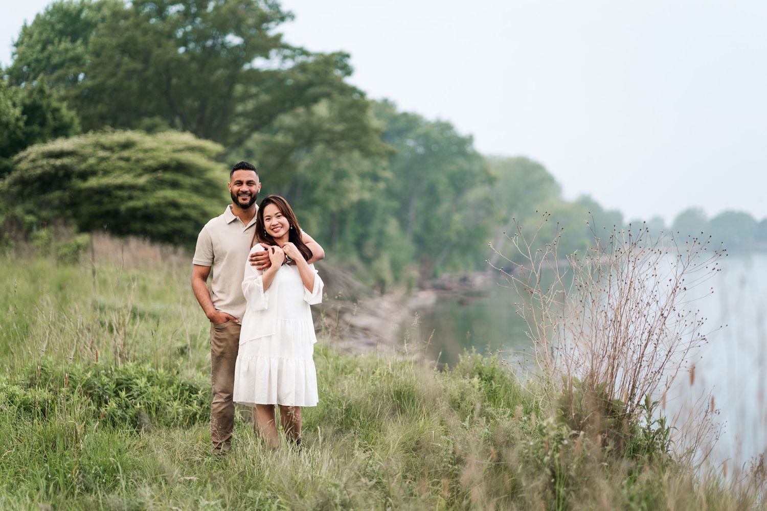 A couple poses together on a grassy hillside overlooking a lake.
Niagara engagement photos.