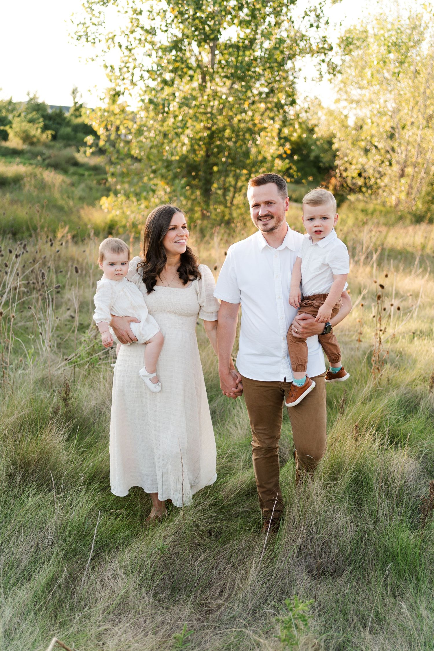 Family poses together in a sunlit field wearing coordinated white and brown outfits.
Niagara family photos.
