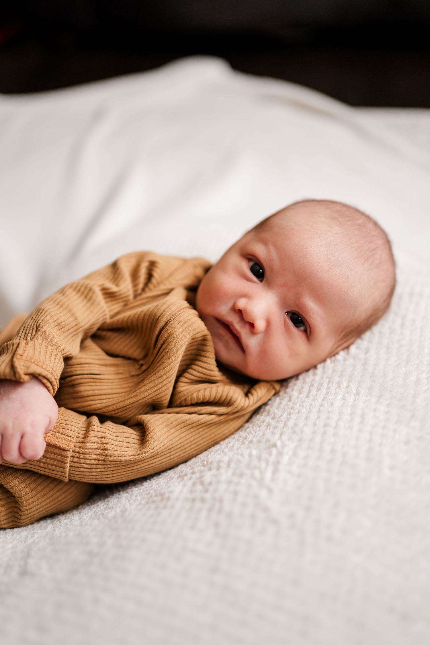 Baby in brown knit outfit lying on textured white bedding.
Niagara newborn photos.