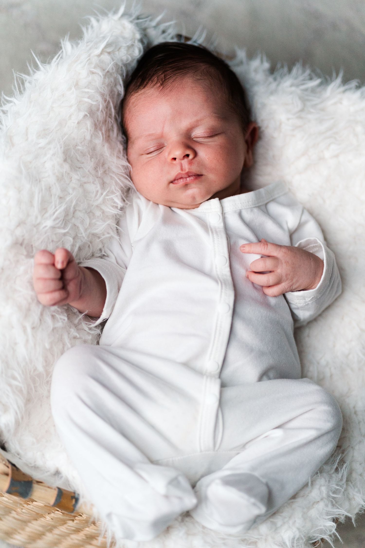 Newborn in white sleeper resting on plush white fur blanket.
Niagara newborn photos.