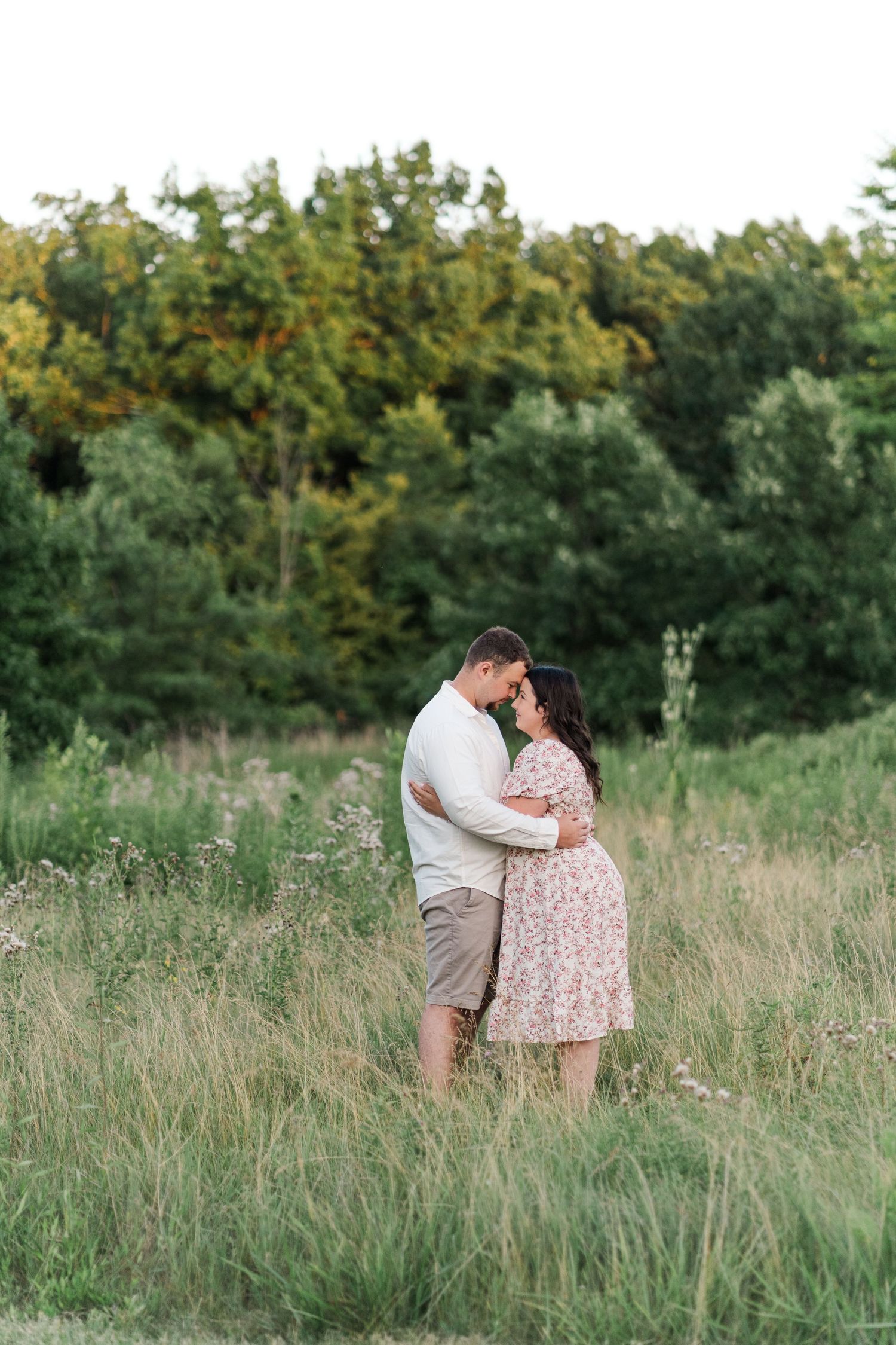 A romantic couple embraces in a sunlit meadow with tall grass and trees.
Niagara engagement photos.