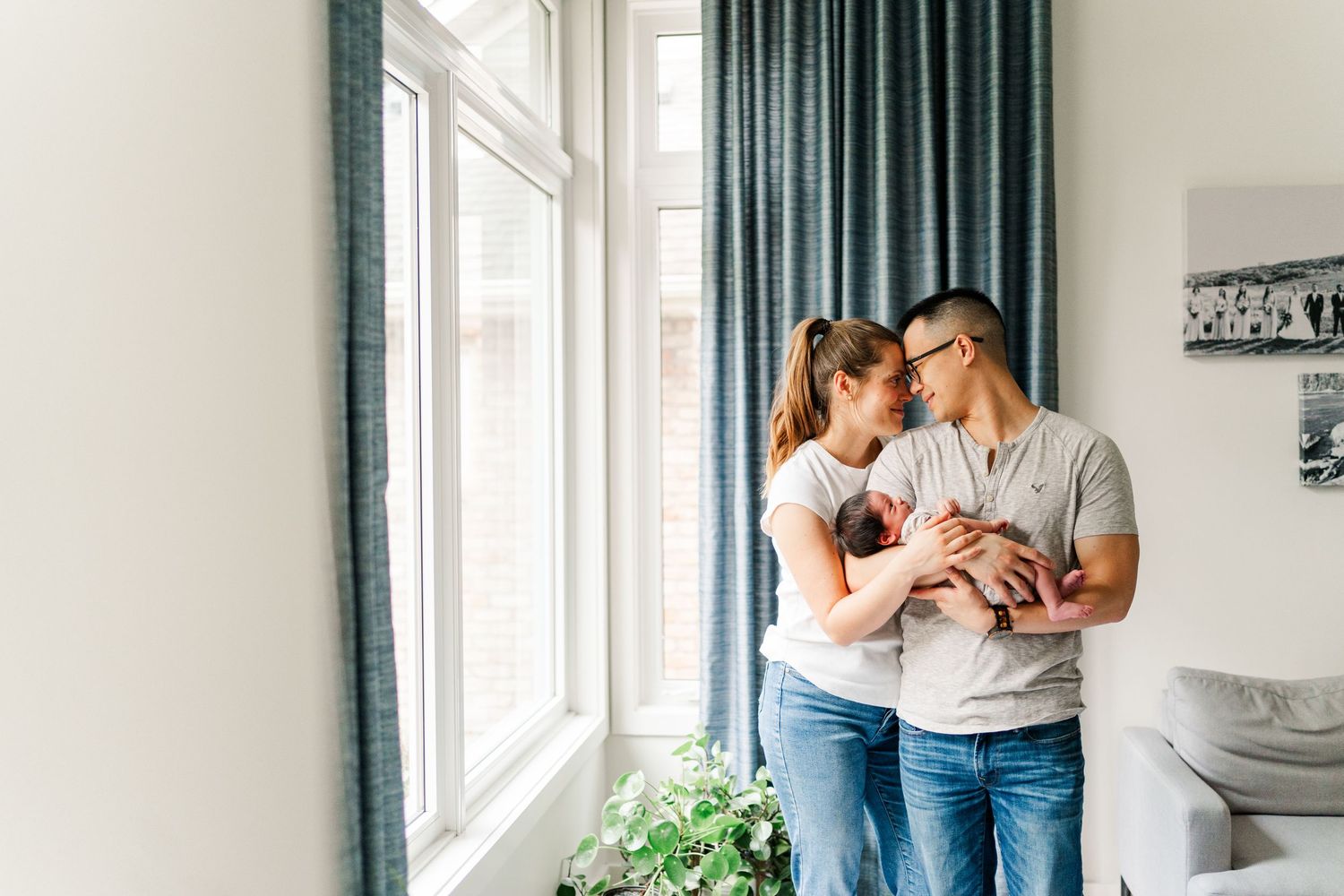 Couple shares intimate moments in bright modern room with teal curtains. Niagara Newborn photos.