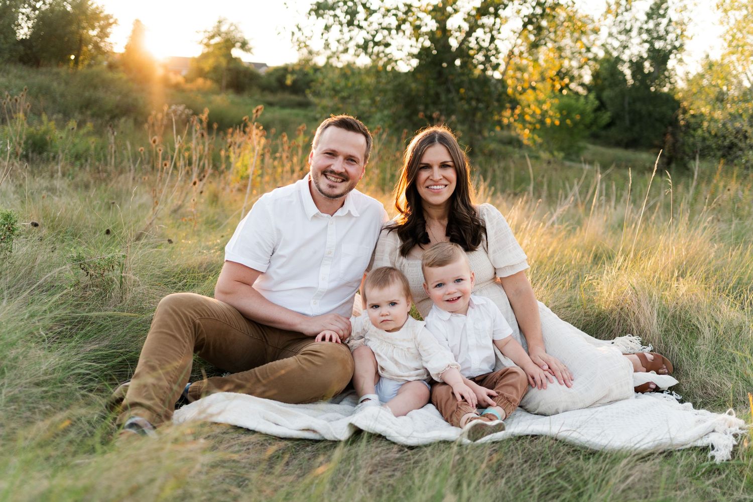 Family sitting together on a blanket in a grassy field during golden hour.
Niagara family photos.