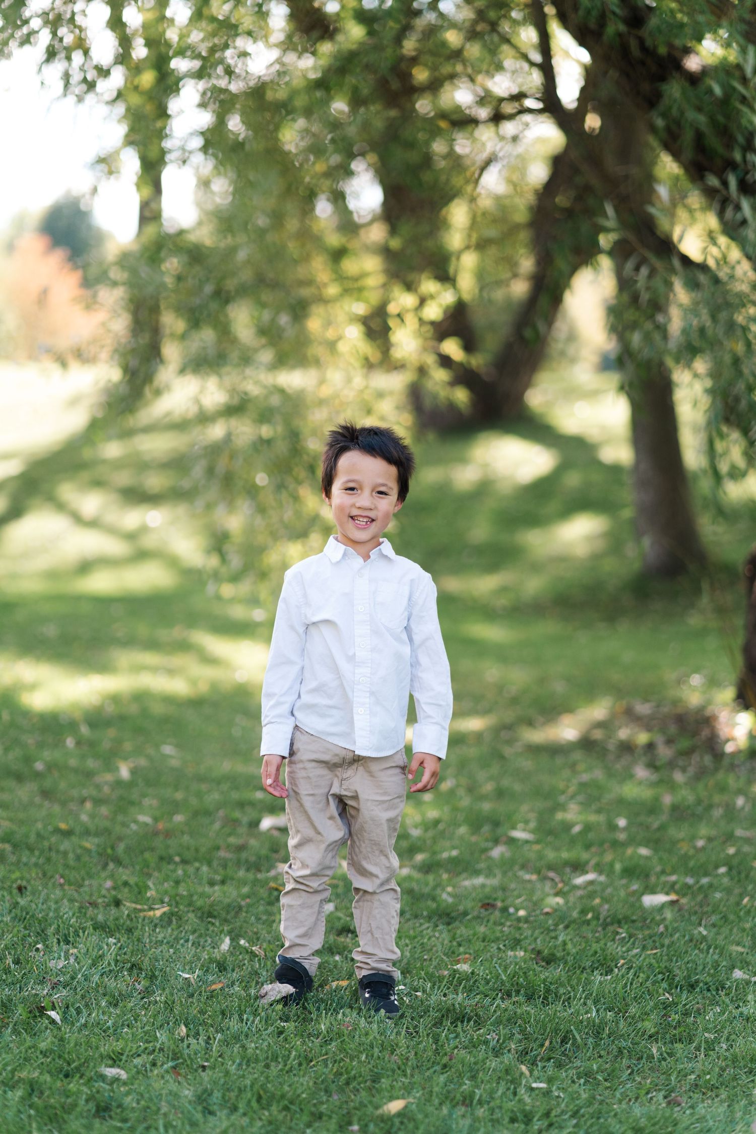 Child in white button-down shirt and khaki pants stands on grass with trees in background.
Niagara family photos.