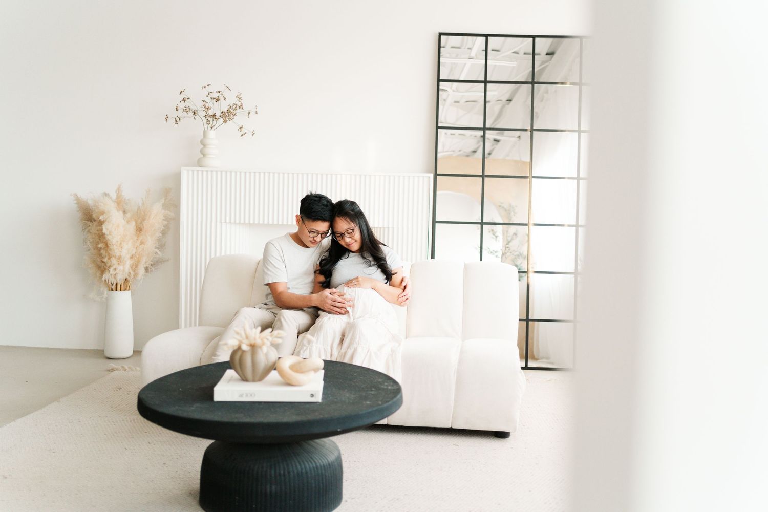 A minimalist white interior design scene with a decorative vase and pampas grass against a bright window.